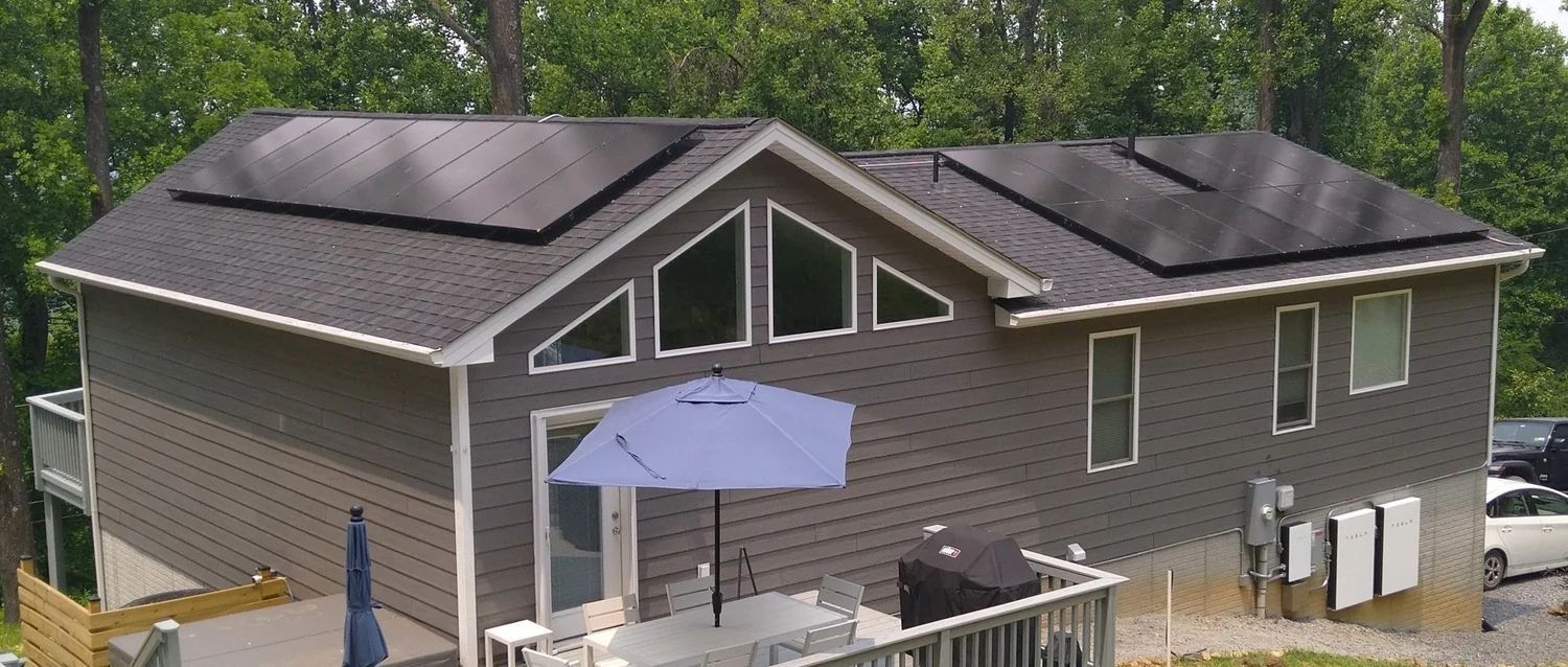 House with solar panels on the roof, a deck, and a blue umbrella in the yard.