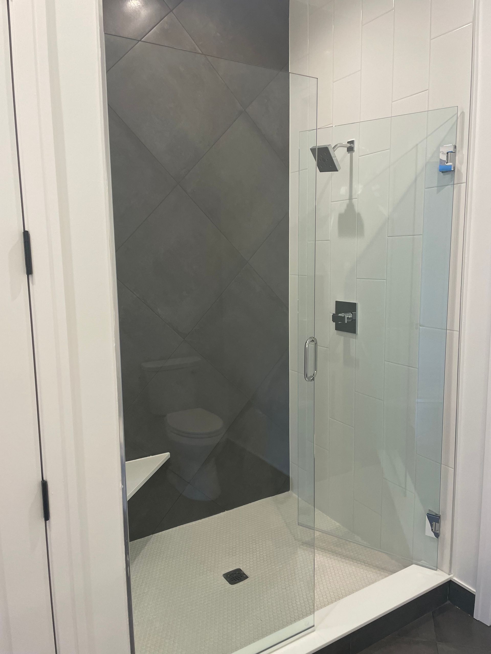 Modern bathroom shower with clear glass door, white tile floor, and dark tiled wall