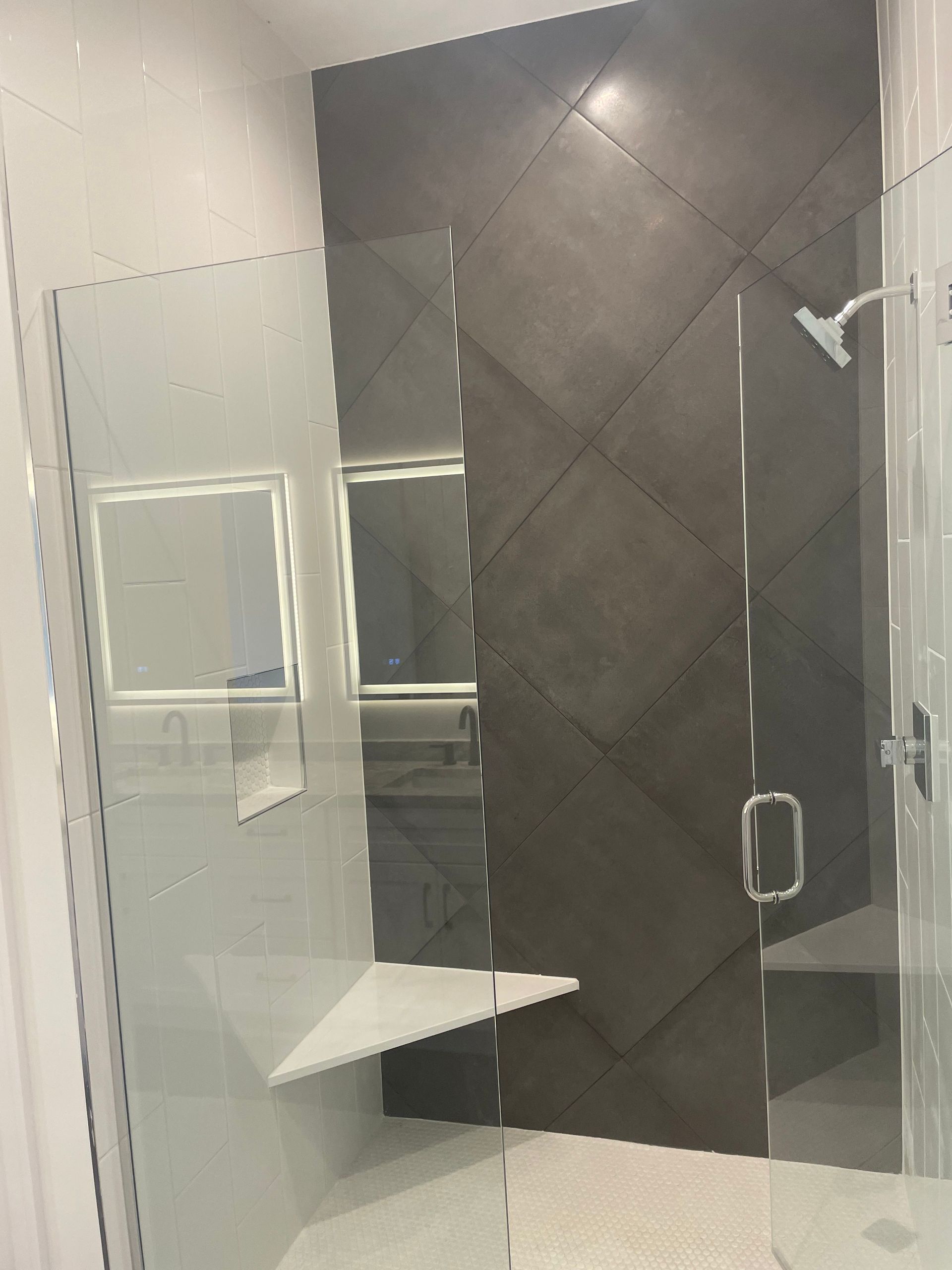 Modern bathroom shower with glass doors, dark tiled accent wall, and built-in shelf.