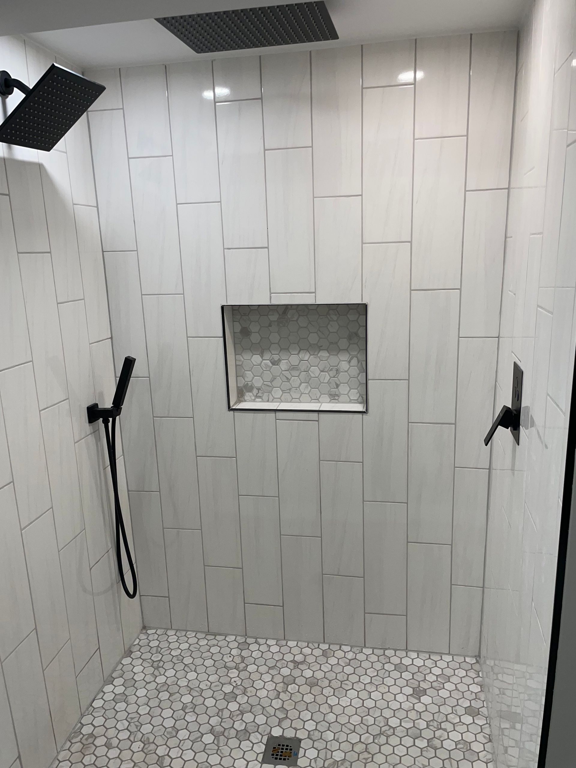 Empty tiled shower stall with two black grab bars and a centered recessed shelf.