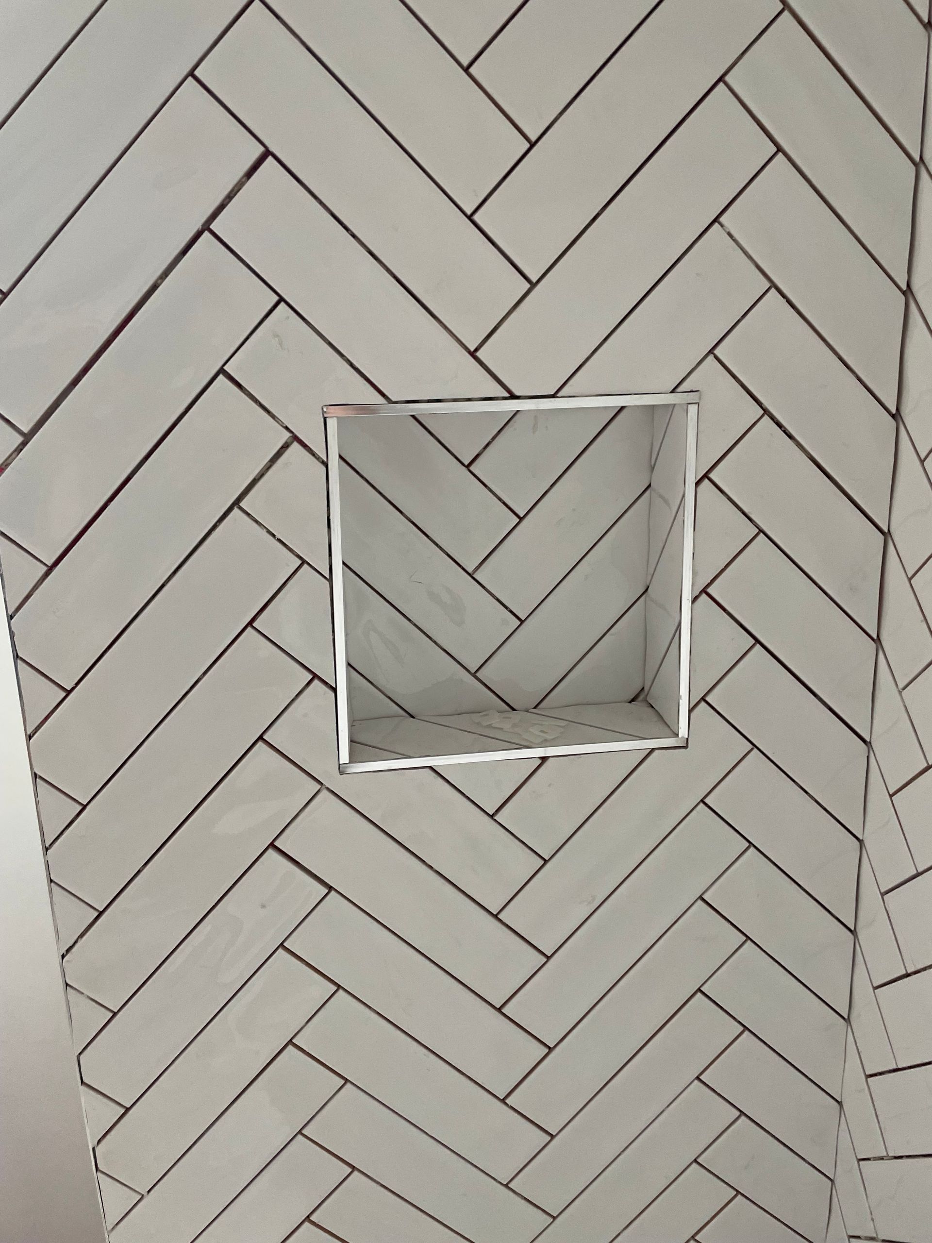 White herringbone tile wall with a small square recessed opening in the center