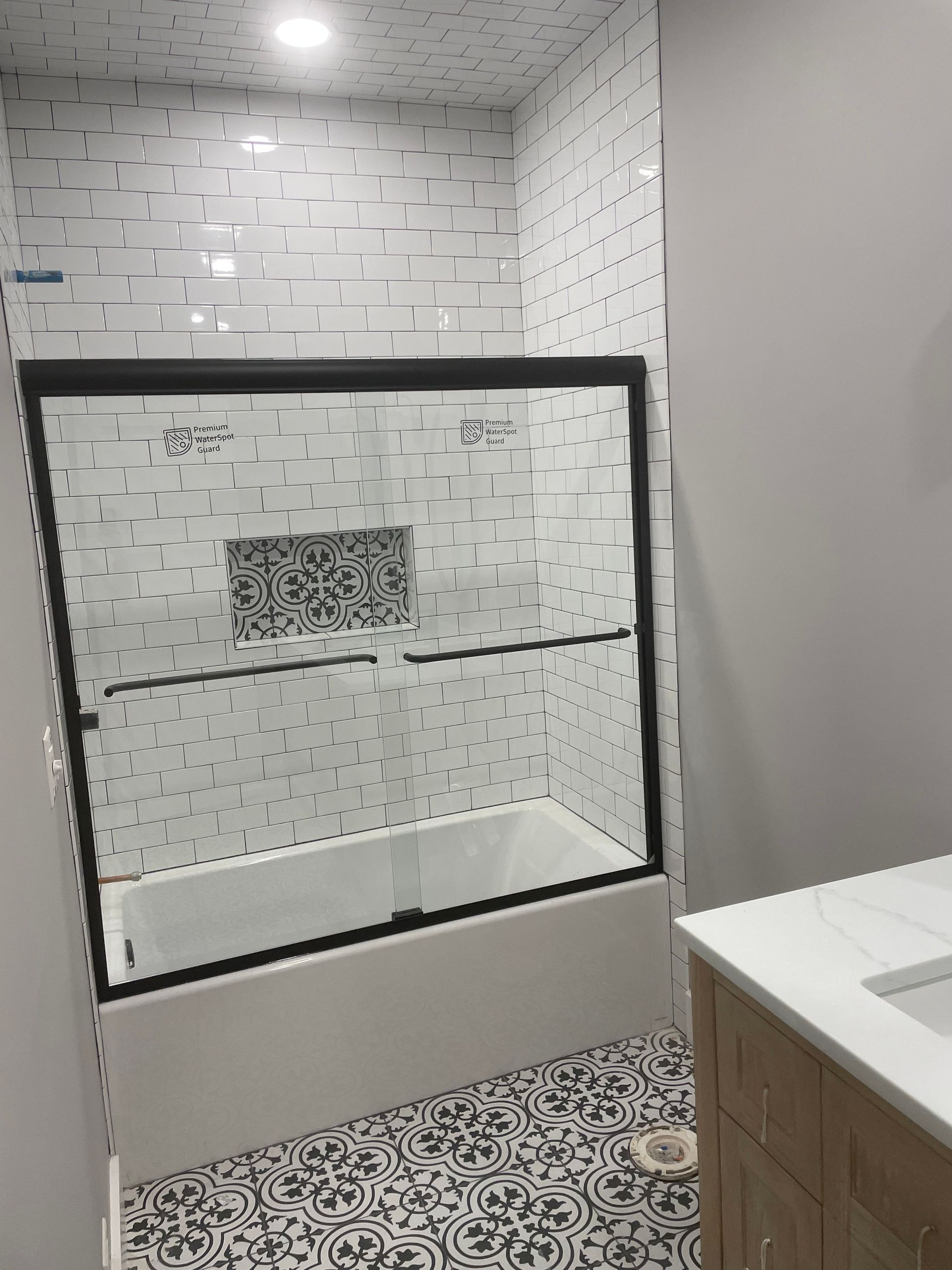 Modern bathroom with glass shower enclosure, patterned tile floor, and white-tiled walls.