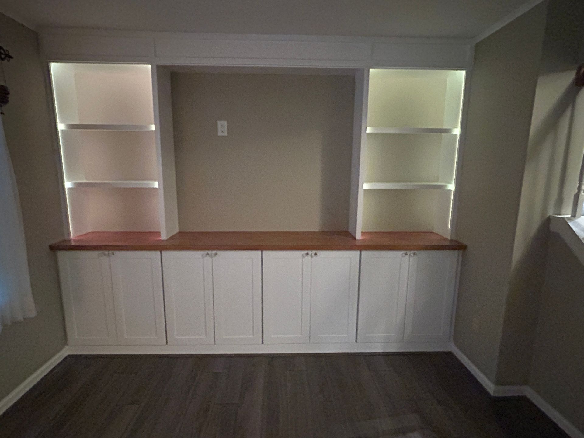 Built-in cabinets with wood countertop and lit display shelves in a small room