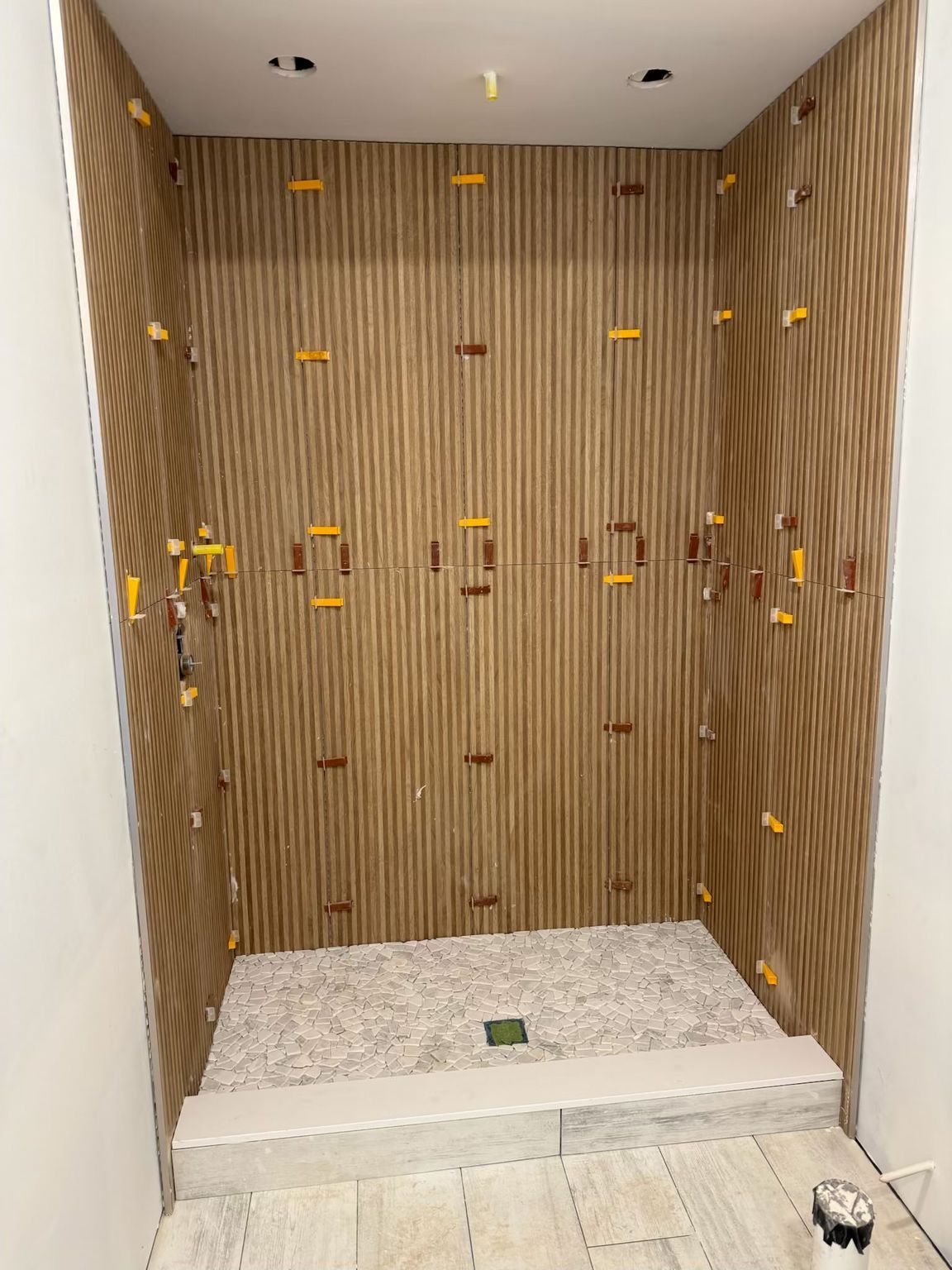 Empty tiled shower stall with wood-look walls, built-in shelf, and white pebble shower floor.