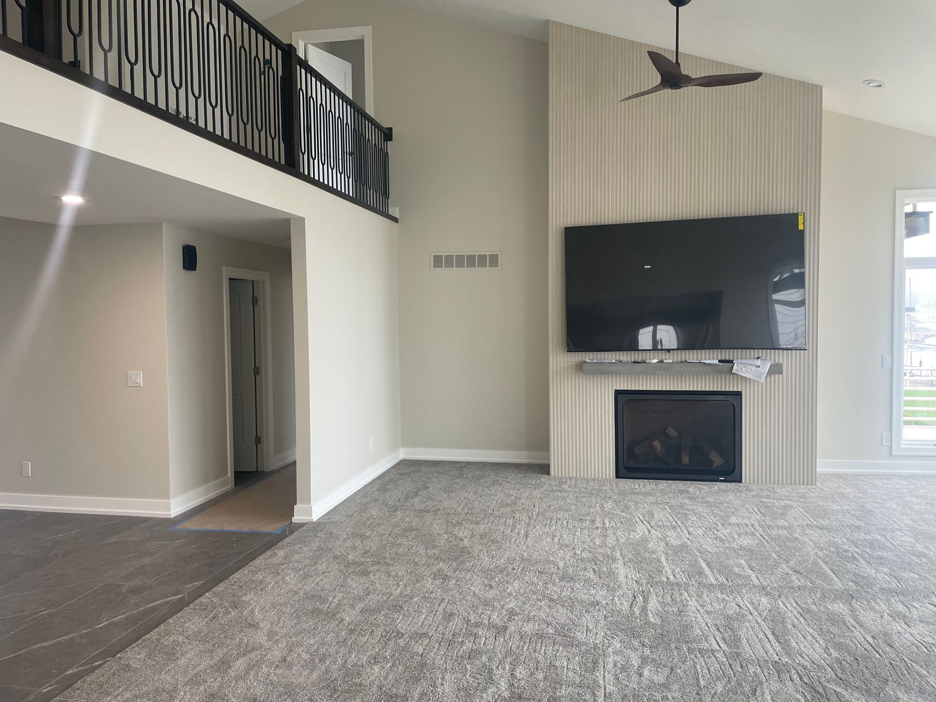 Empty living room with carpet, fireplace, wall-mounted TV, and loft railing overhead