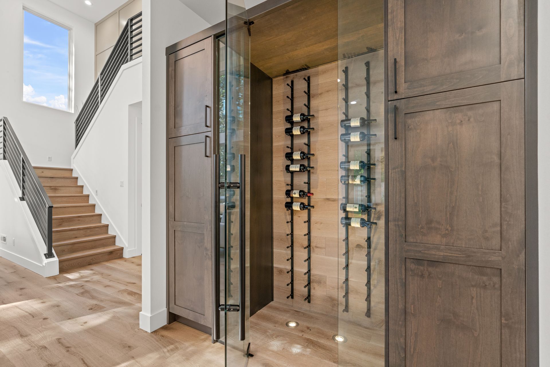 A wine cellar with a glass door and a staircase in the background.