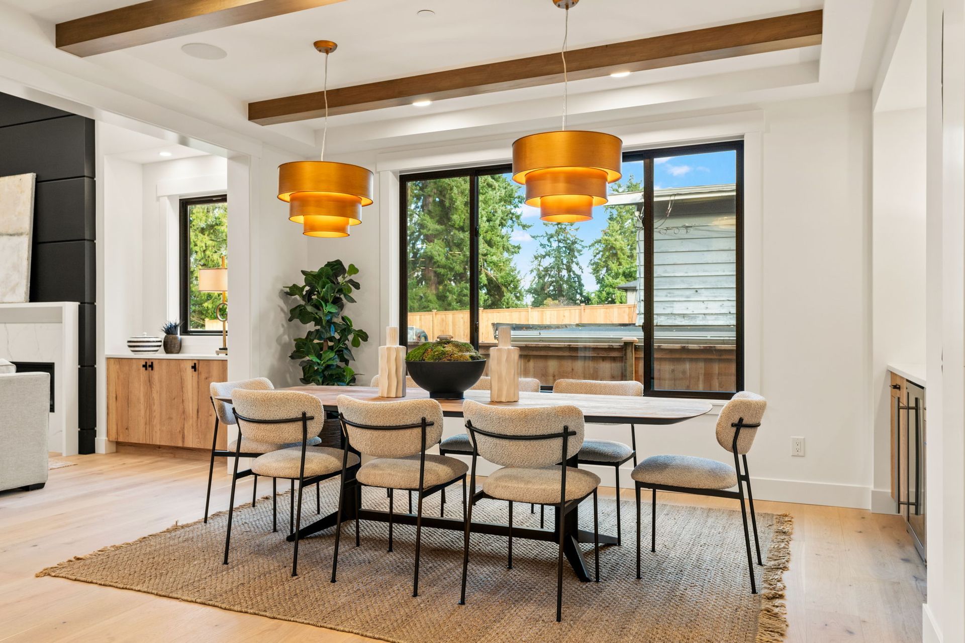 Dining room with table, chairs, gold light fixtures, and windows overlooking greenery.