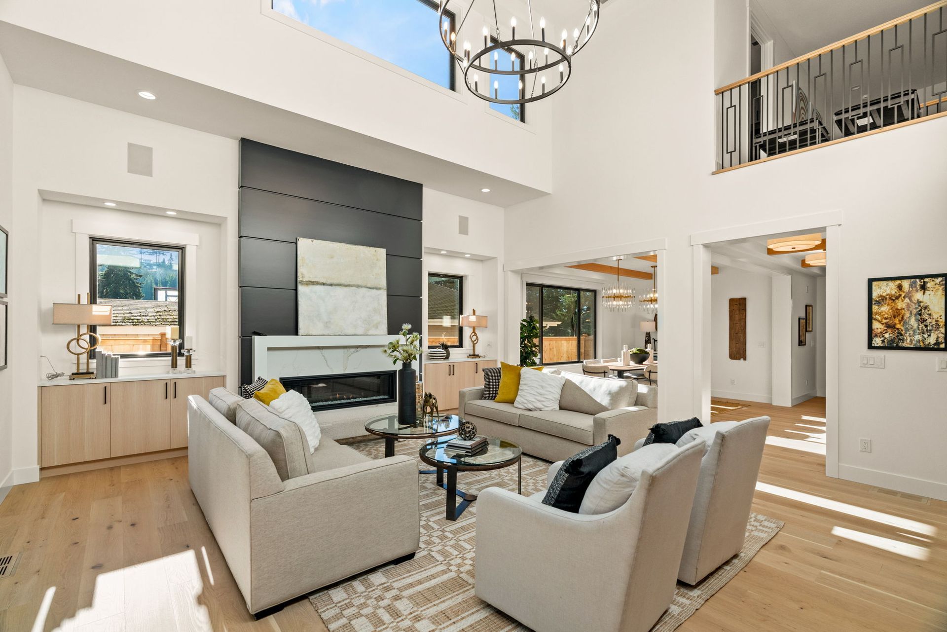 Spacious living room with high ceilings, fireplace, and two levels. Light wood floors and furniture.