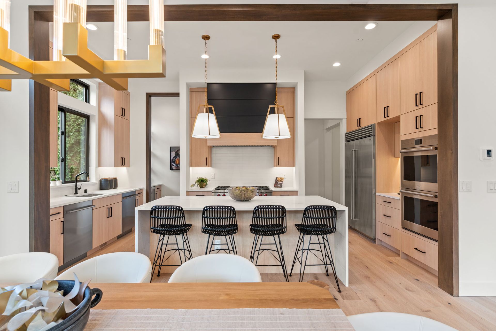 Modern kitchen with light wood cabinets, white island with black stools, and stainless steel appliances.