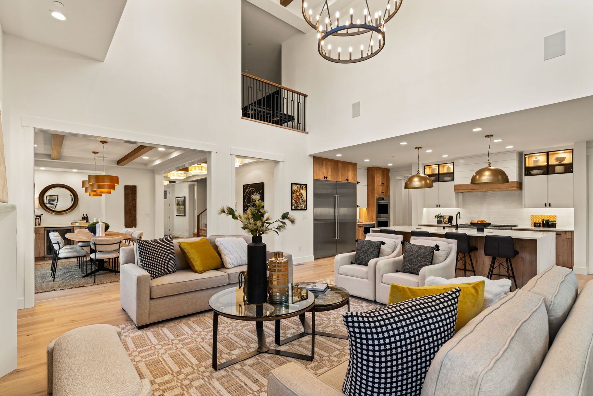 Spacious living room with high ceilings, open to kitchen and dining area. Neutral colors, modern furniture, and a chandelier.