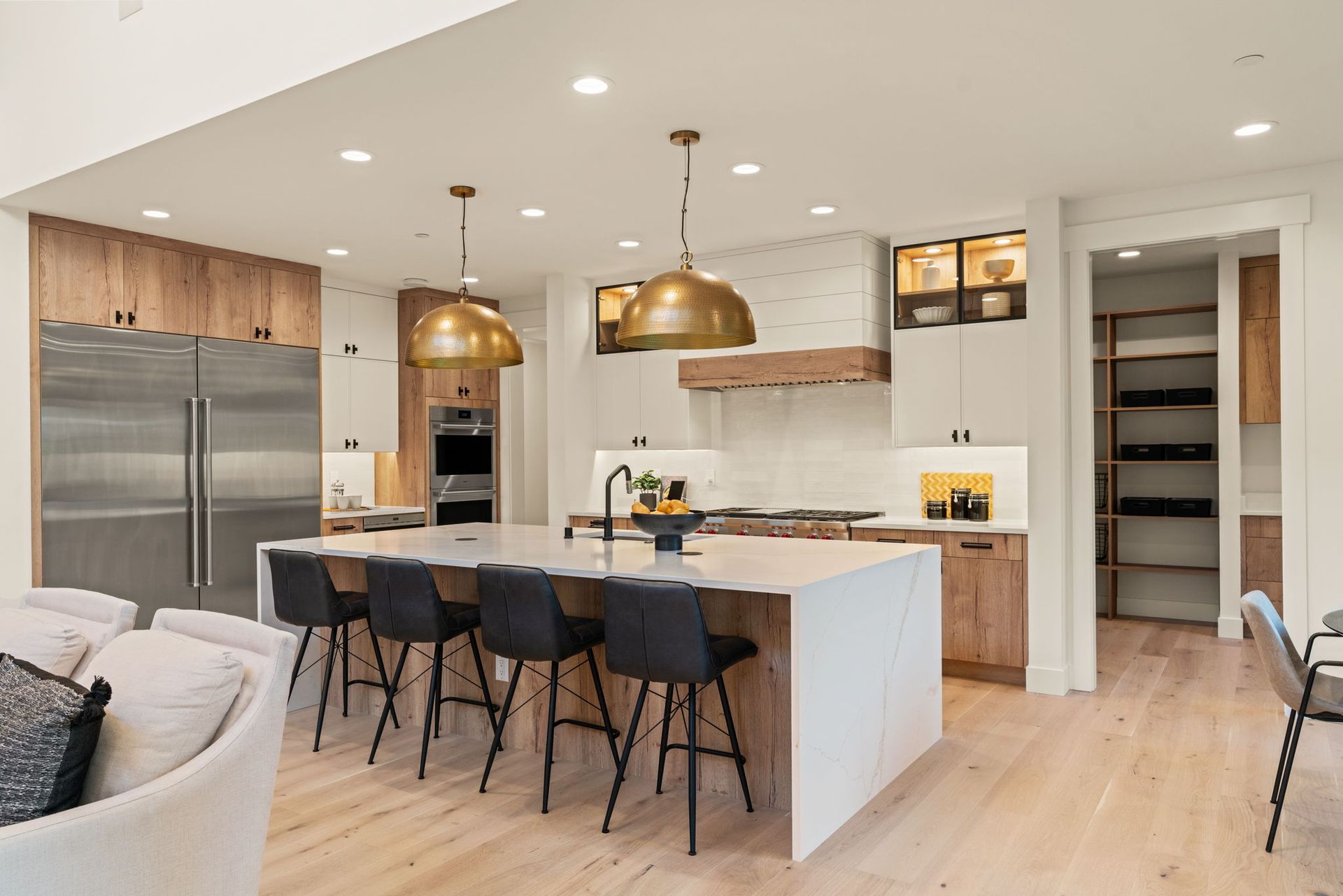 Modern kitchen with island, pendant lights, wooden cabinets, stainless steel refrigerator, and bar stools.