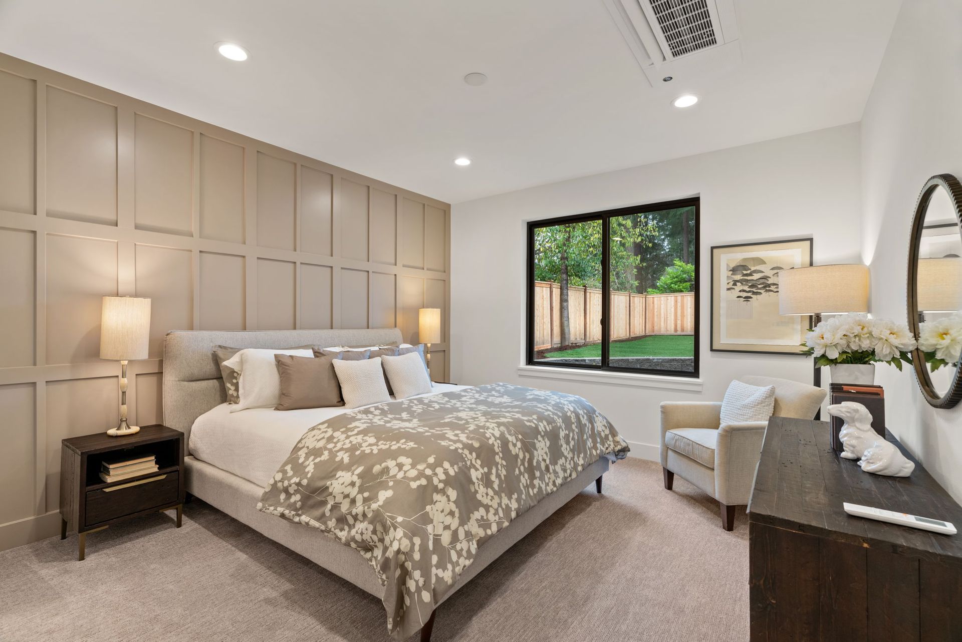 A bedroom with a bed, chair, dresser, mirror and window.