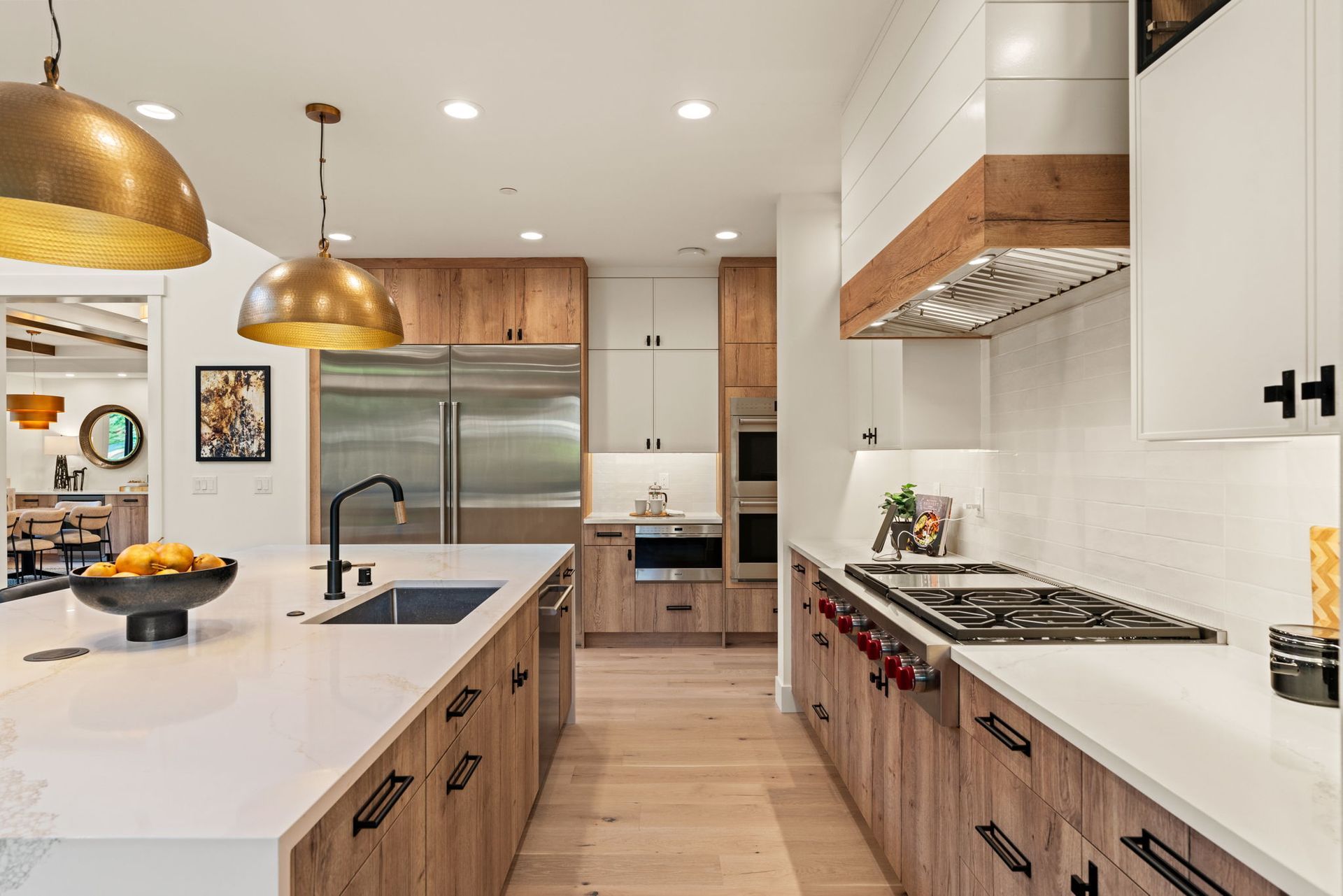 Modern kitchen with white countertops, wooden cabinets, stainless steel appliances, and gold pendant lights.