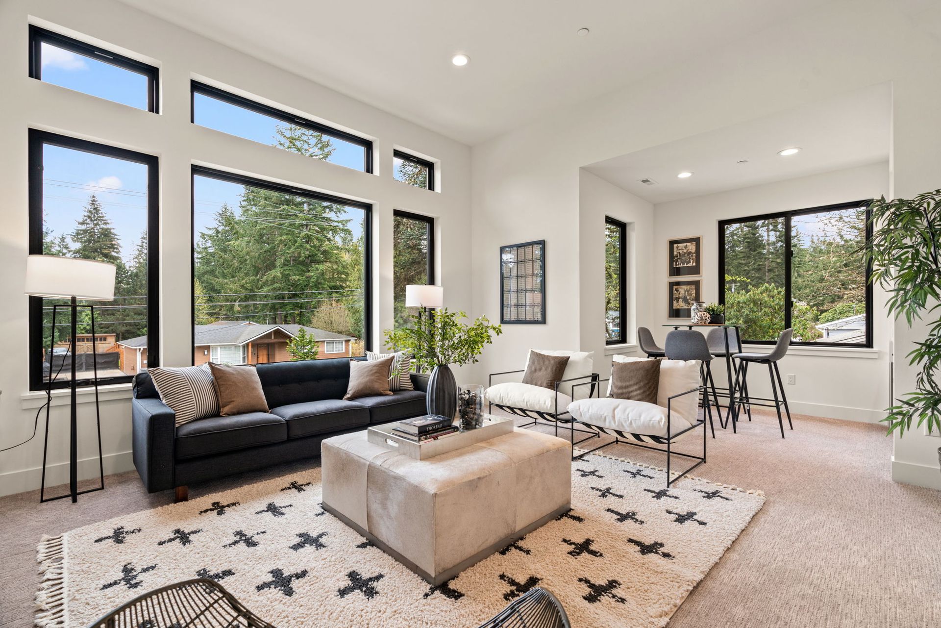A bonus room with a black couch, white chairs, and a rug.