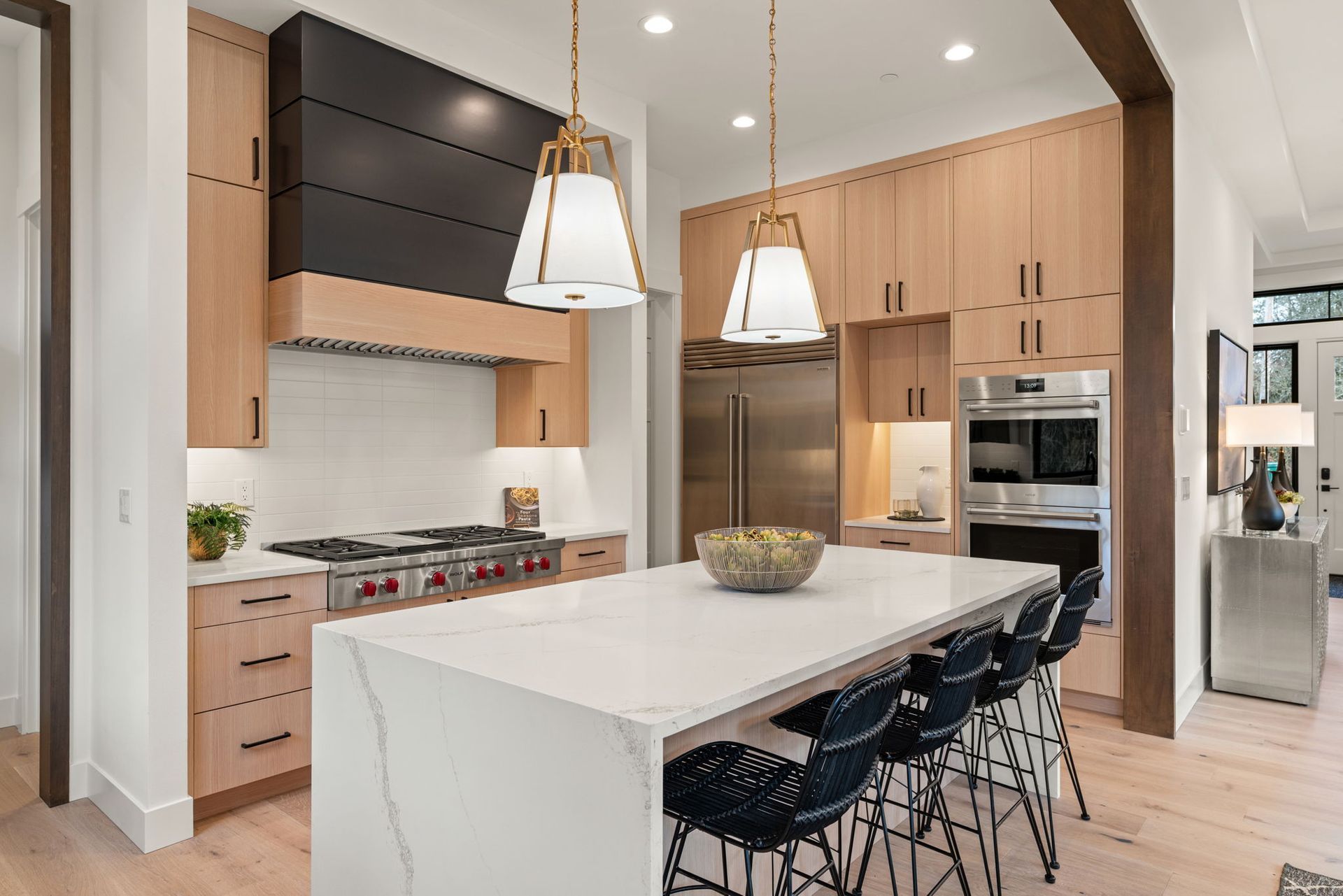 Modern kitchen with light wood cabinets, white island, and black range hood.