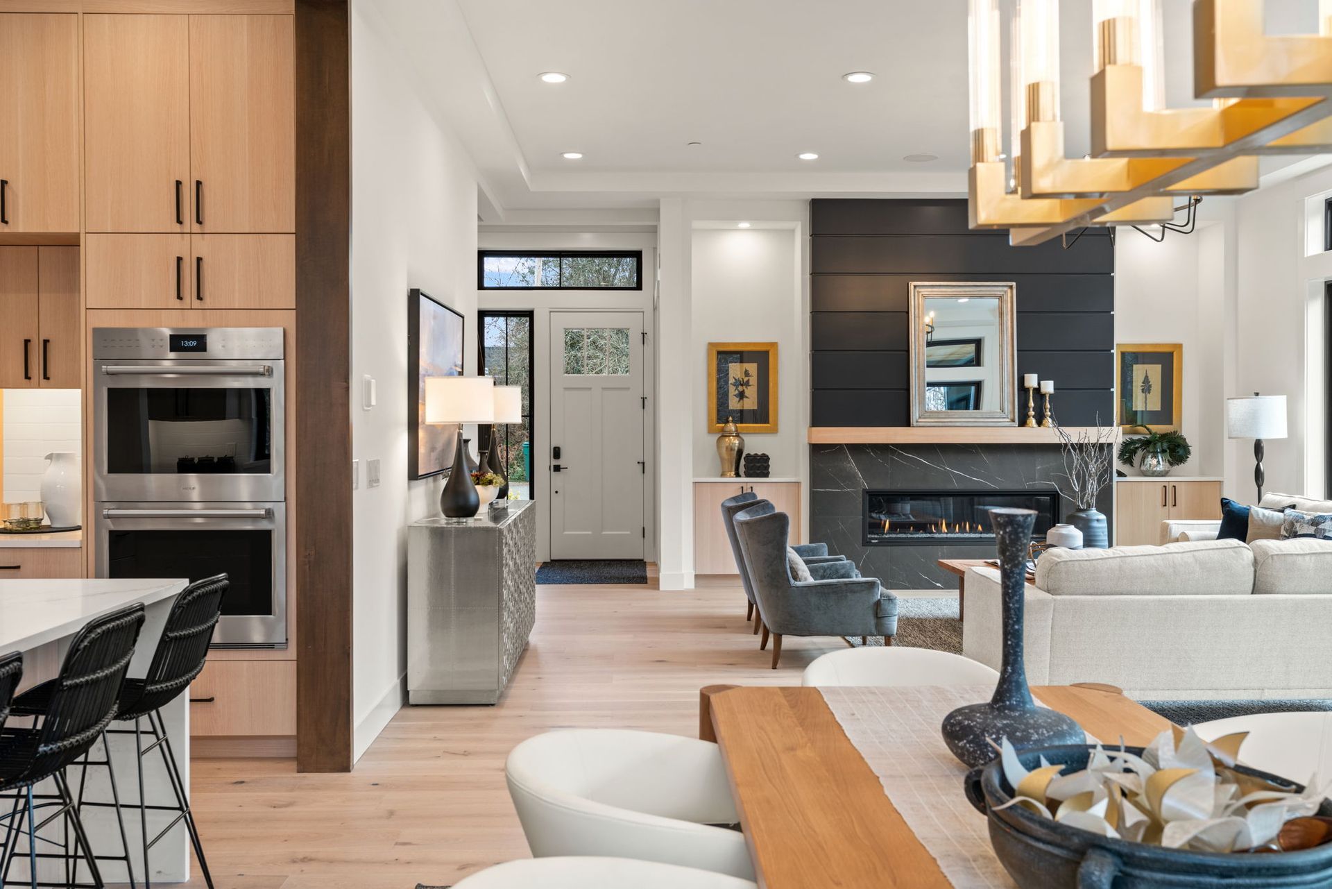 Bright, modern home interior. Kitchen with island, dining area, fireplace, and entryway visible.