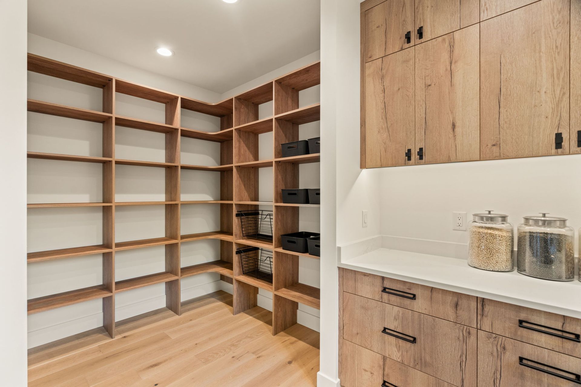 Wooden pantry with shelves and cabinets; white countertop with jars.