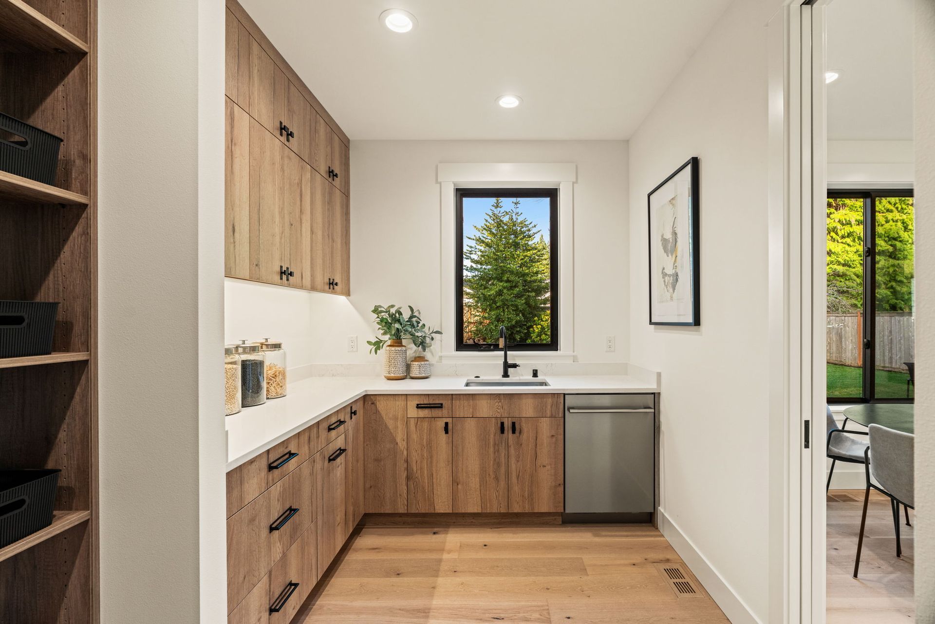 Pantry with light wood cabinets, white countertops, window, and a stainless steel dishwasher.