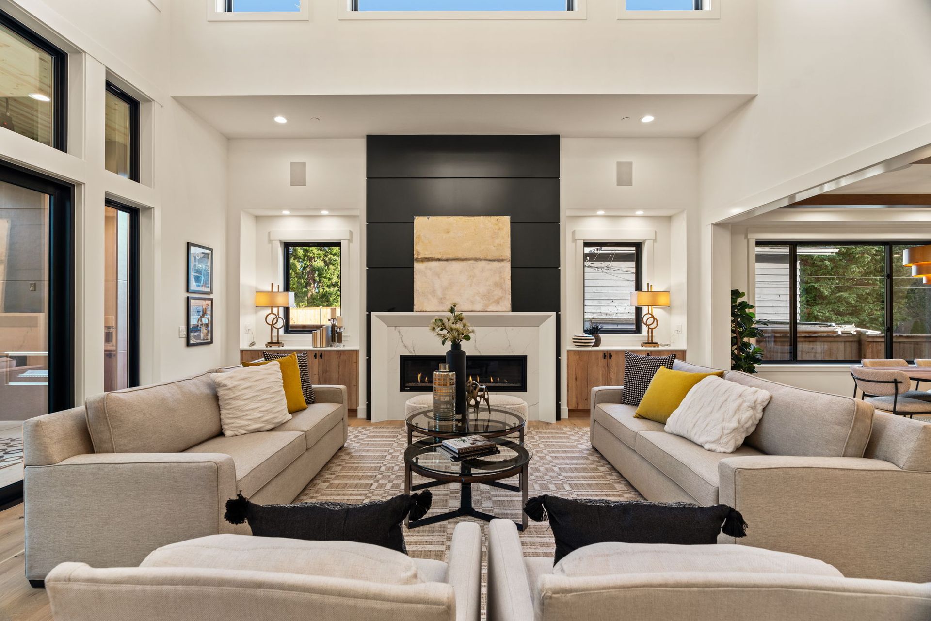 Living room with two sofas, fireplace, and large windows. Beige and black color scheme.