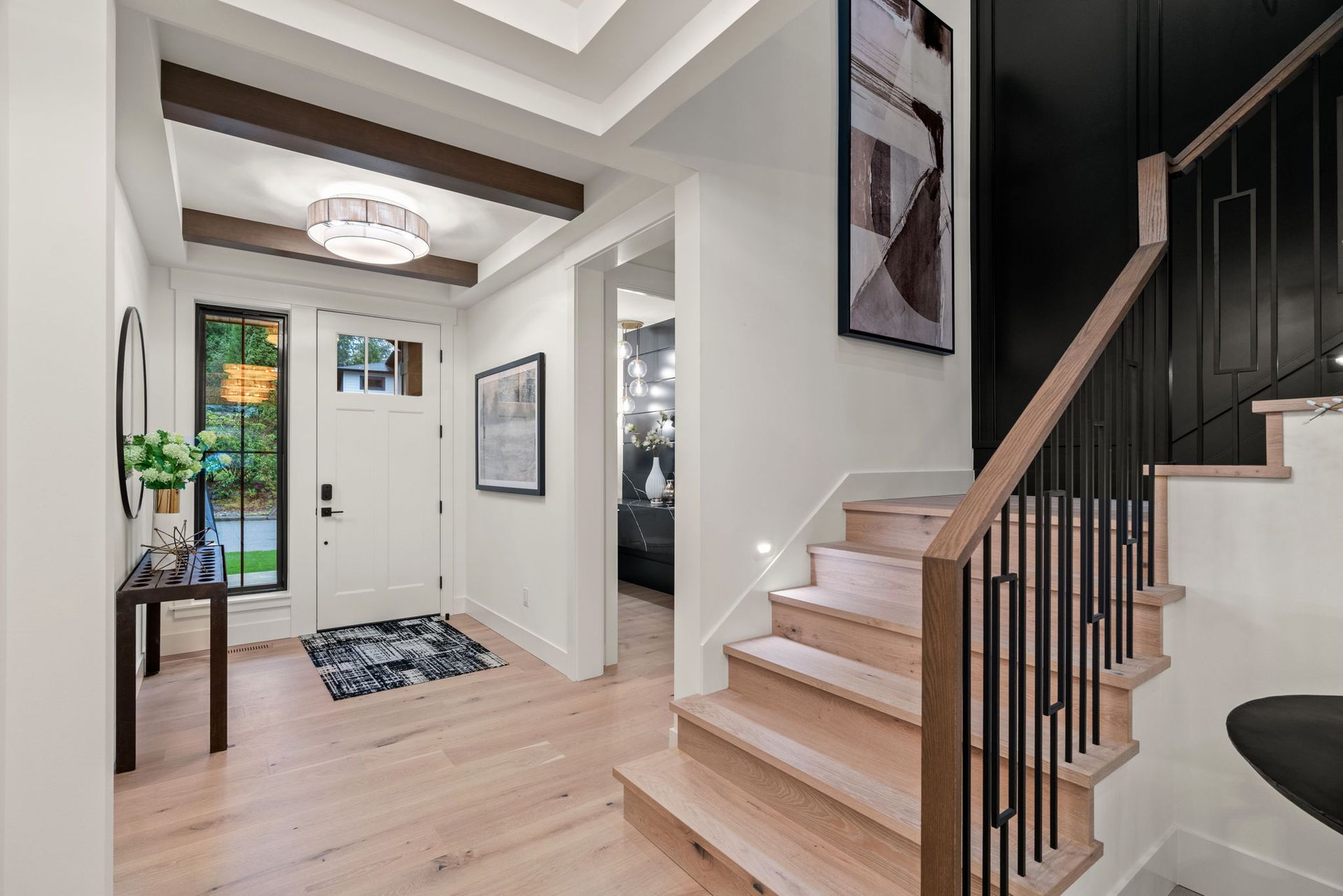 Entryway with stairs and light wood floors. White walls, dark accent wall, chandelier, and a front door.