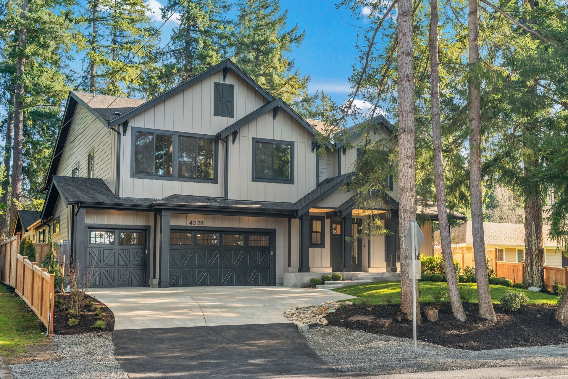Two-story gray house with black trim, two-car garage, and driveway, surrounded by trees.