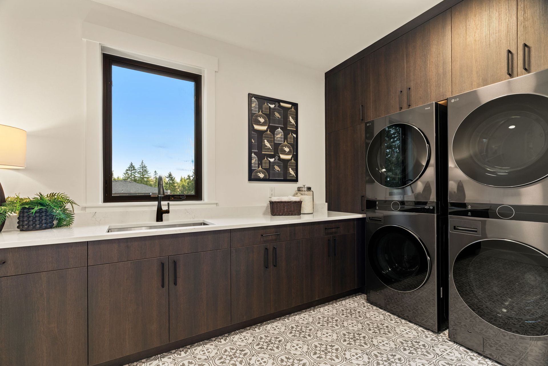 Laundry room with dark wood cabinets, stacked silver washer/dryer, and a window.