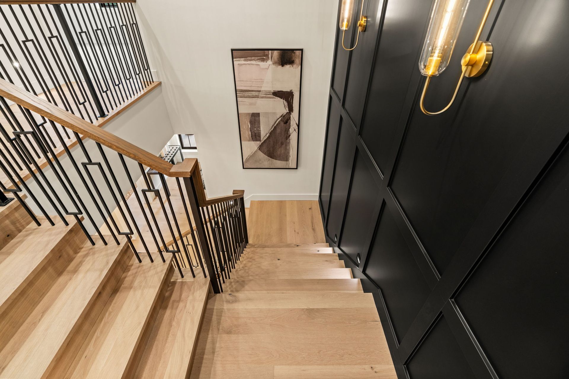 Wooden staircase with black paneling and abstract art. Gold sconces on the wall.