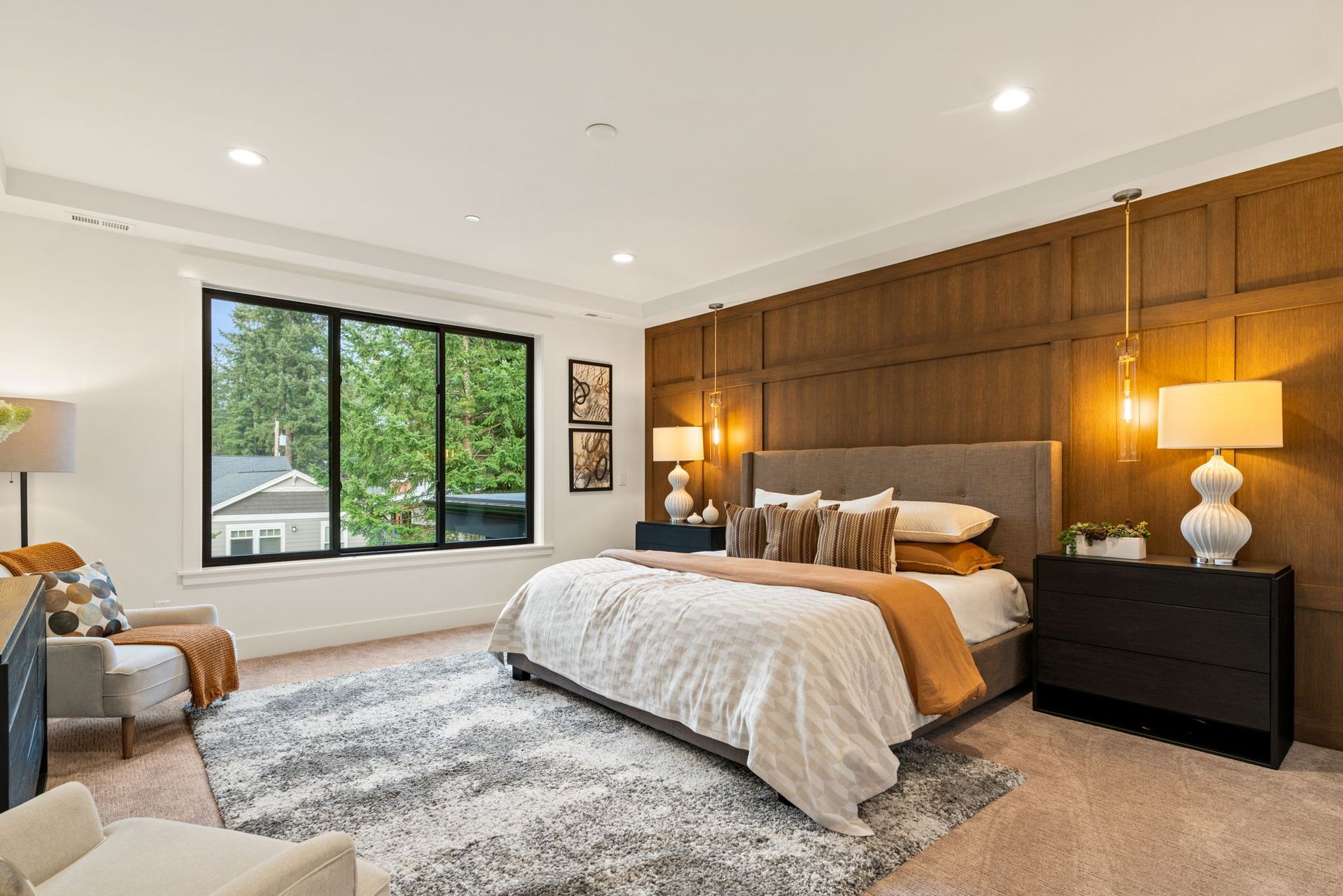 Bedroom with bed, nightstands, rug, window, wood paneling, and pendant lights.