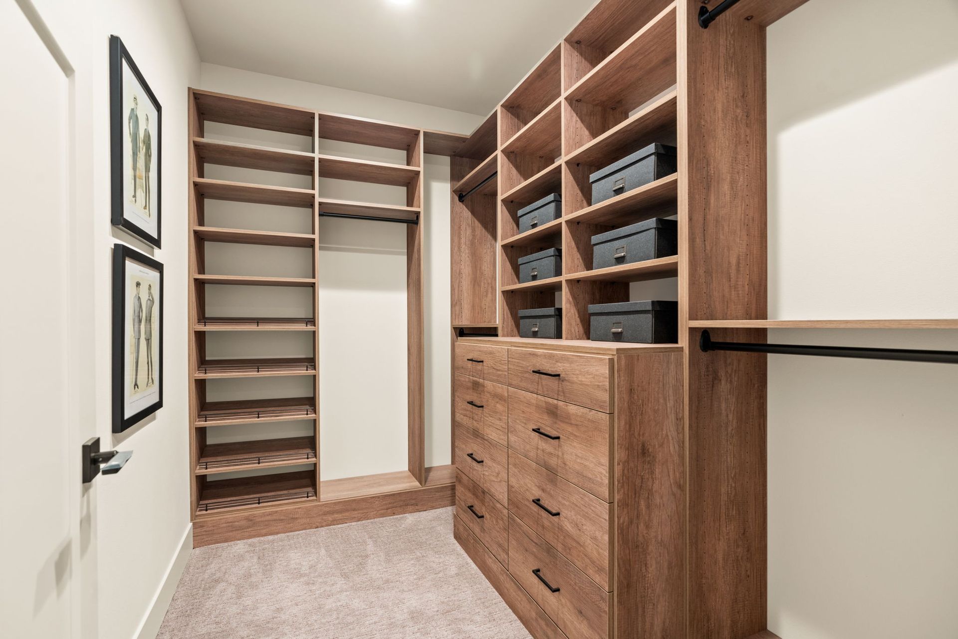 Walk-in closet with wooden shelving, drawers, and hanging rods; gray carpet, white walls, and a door.