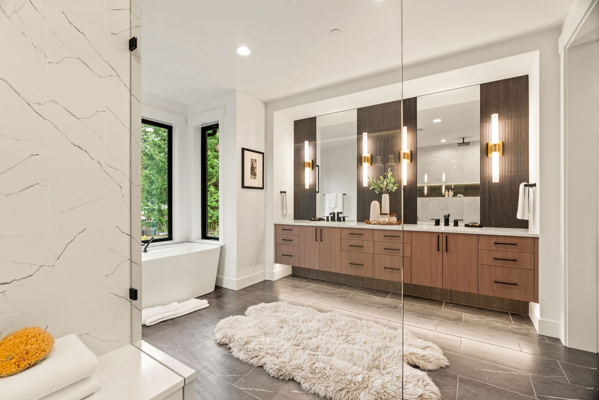 Luxurious bathroom: white bathtub by window, double vanity with mirrors, shaggy rug on dark tiled floor.