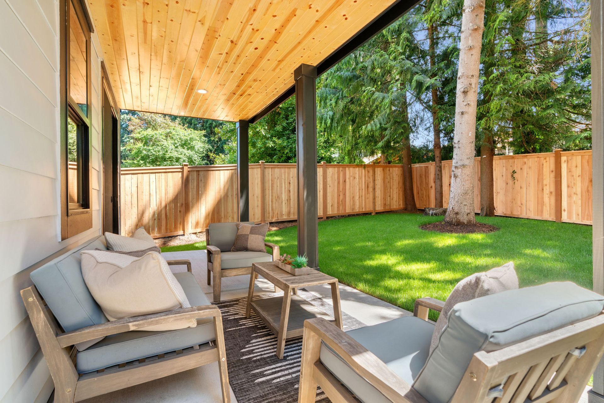 A patio with a couch and chairs under a wooden roof.