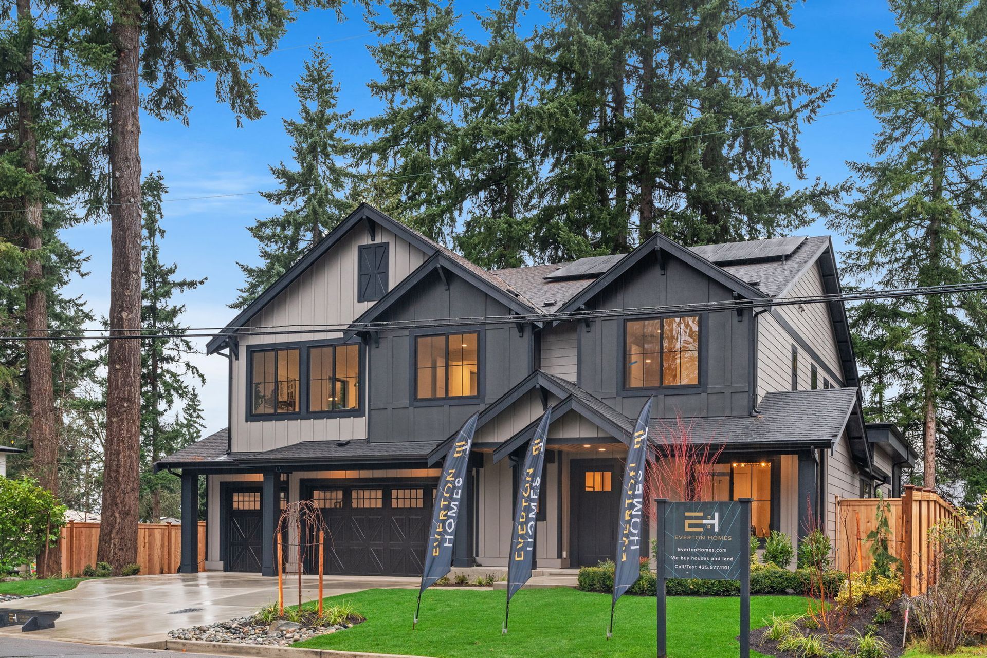 Modern two-story house with dark gray and light tan siding, surrounded by trees and a green lawn.