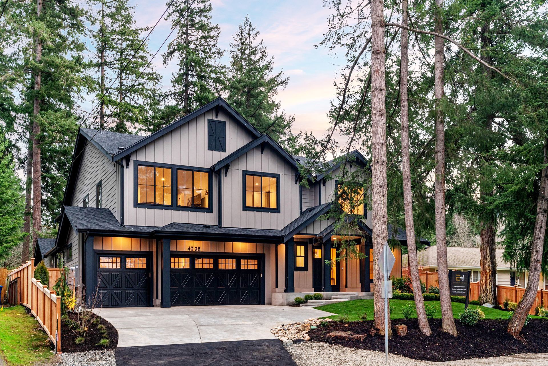 Two-story house with dark gray siding, black garage doors, and a green lawn, surrounded by trees.