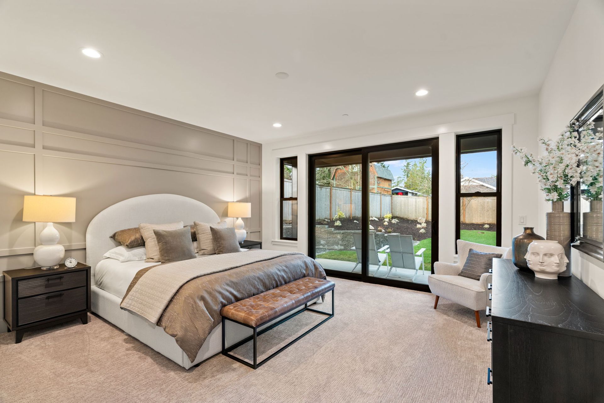 Bedroom with bed, bench, sliding glass door, armchair, and dresser. Neutral color palette.