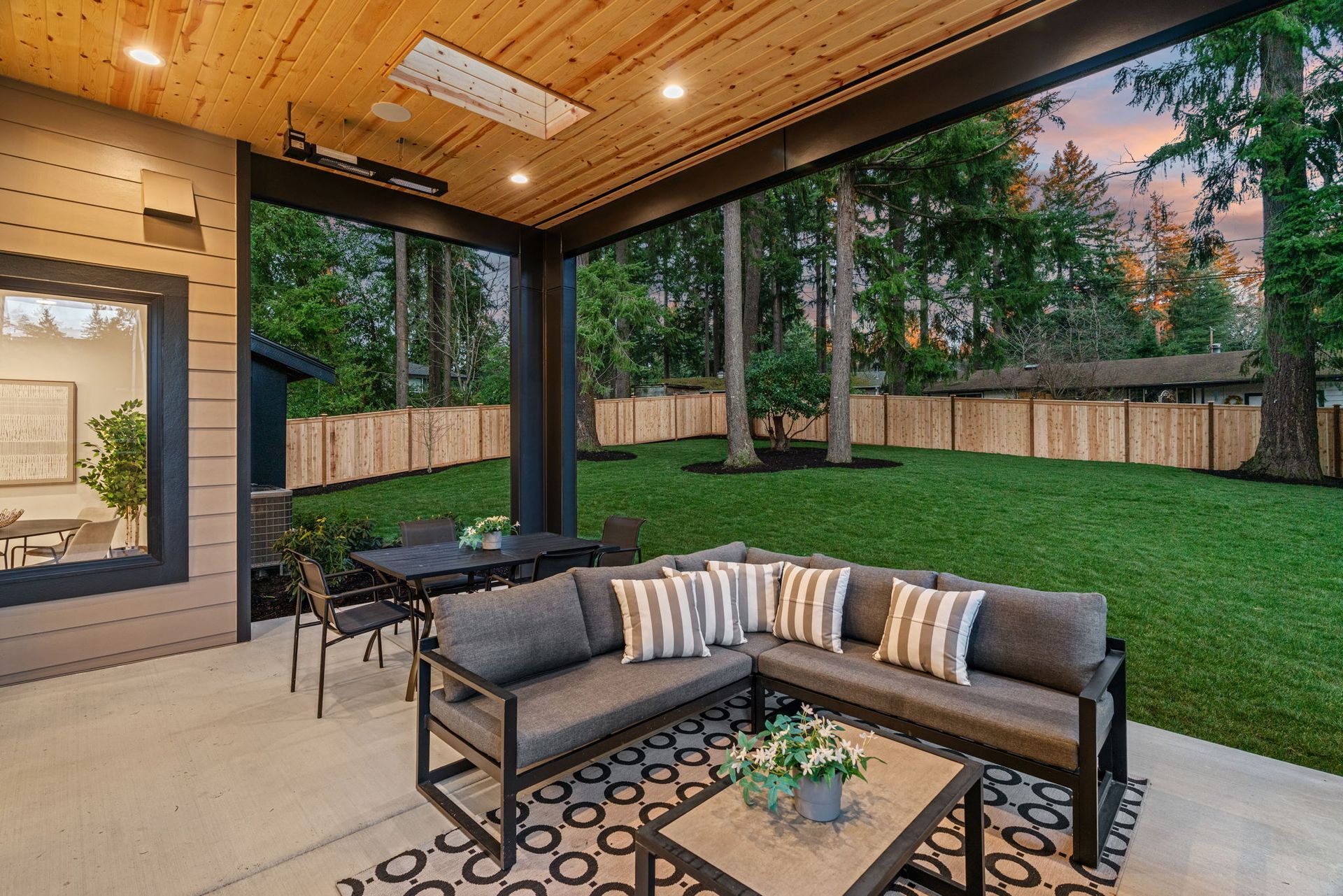 Patio with gray sectional, table, and chairs overlooking a green lawn with a wooden fence.