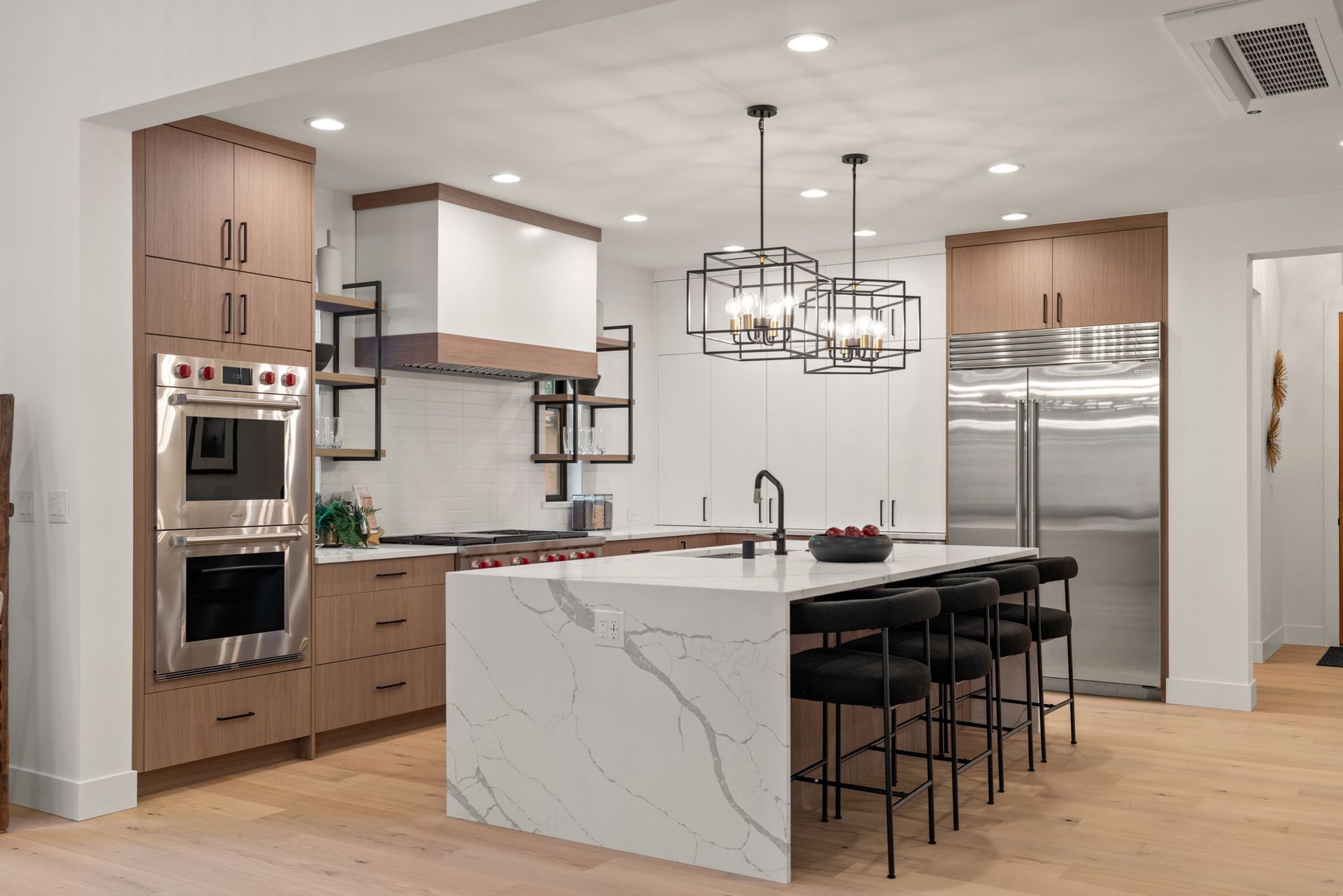 A kitchen with a large island, quartz waterfall counter and stainless steel appliances.