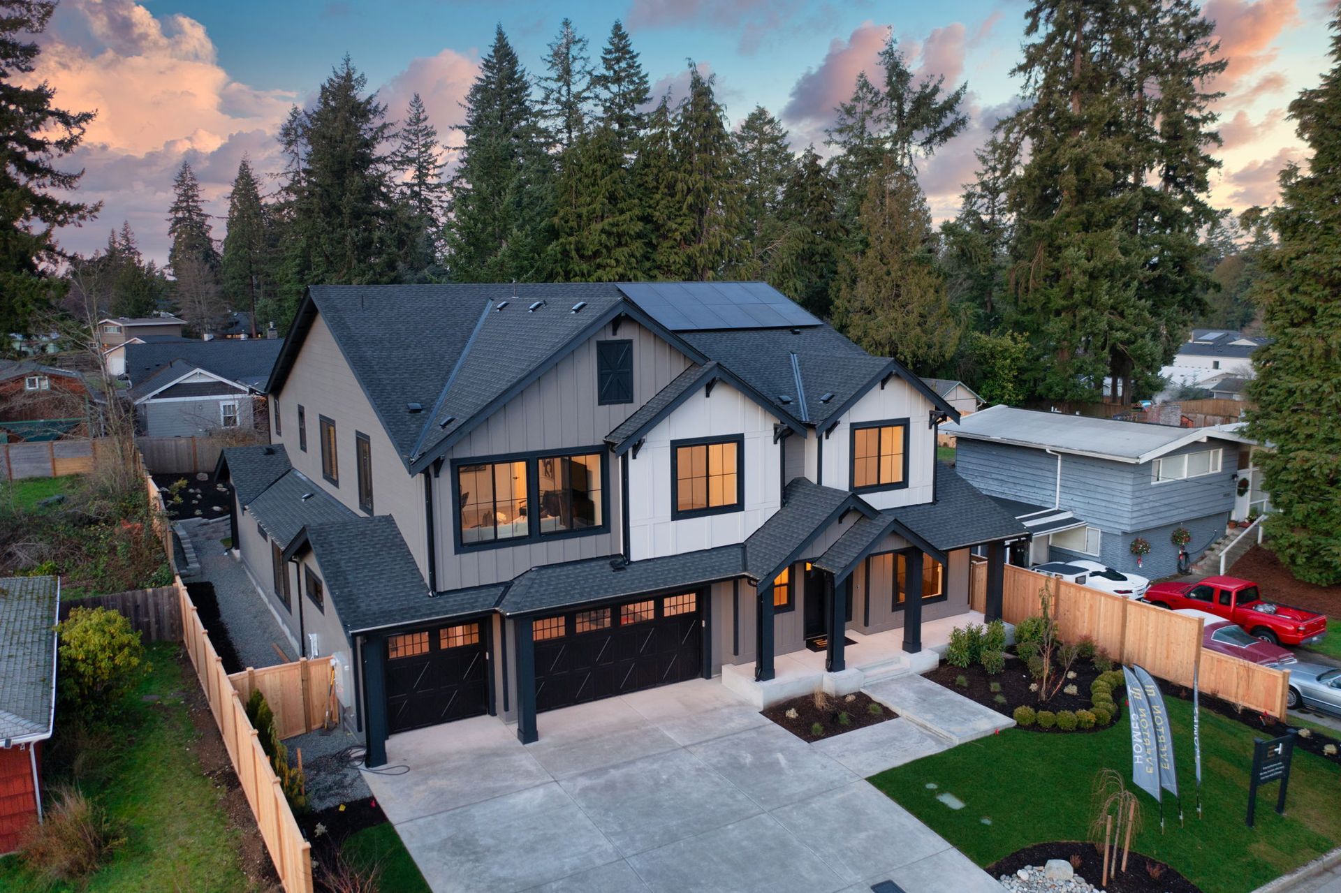 Two-story house with gray and white exterior, black roof and garage doors, surrounded by trees and a driveway.