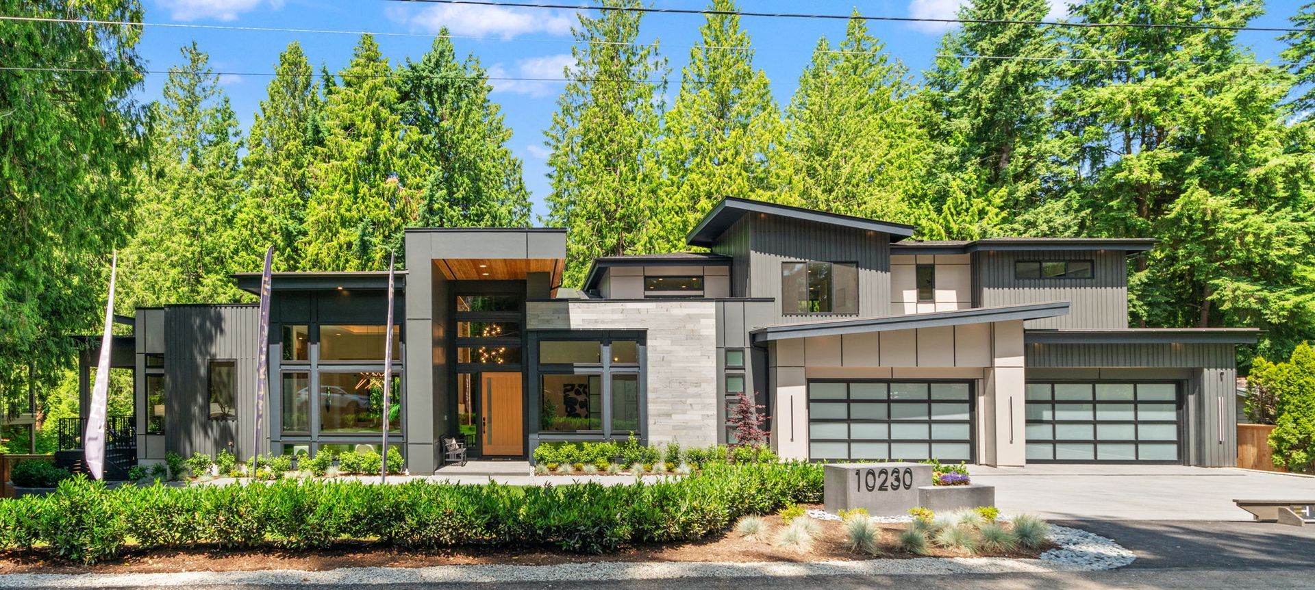 A large modern house with two garages is surrounded by trees.