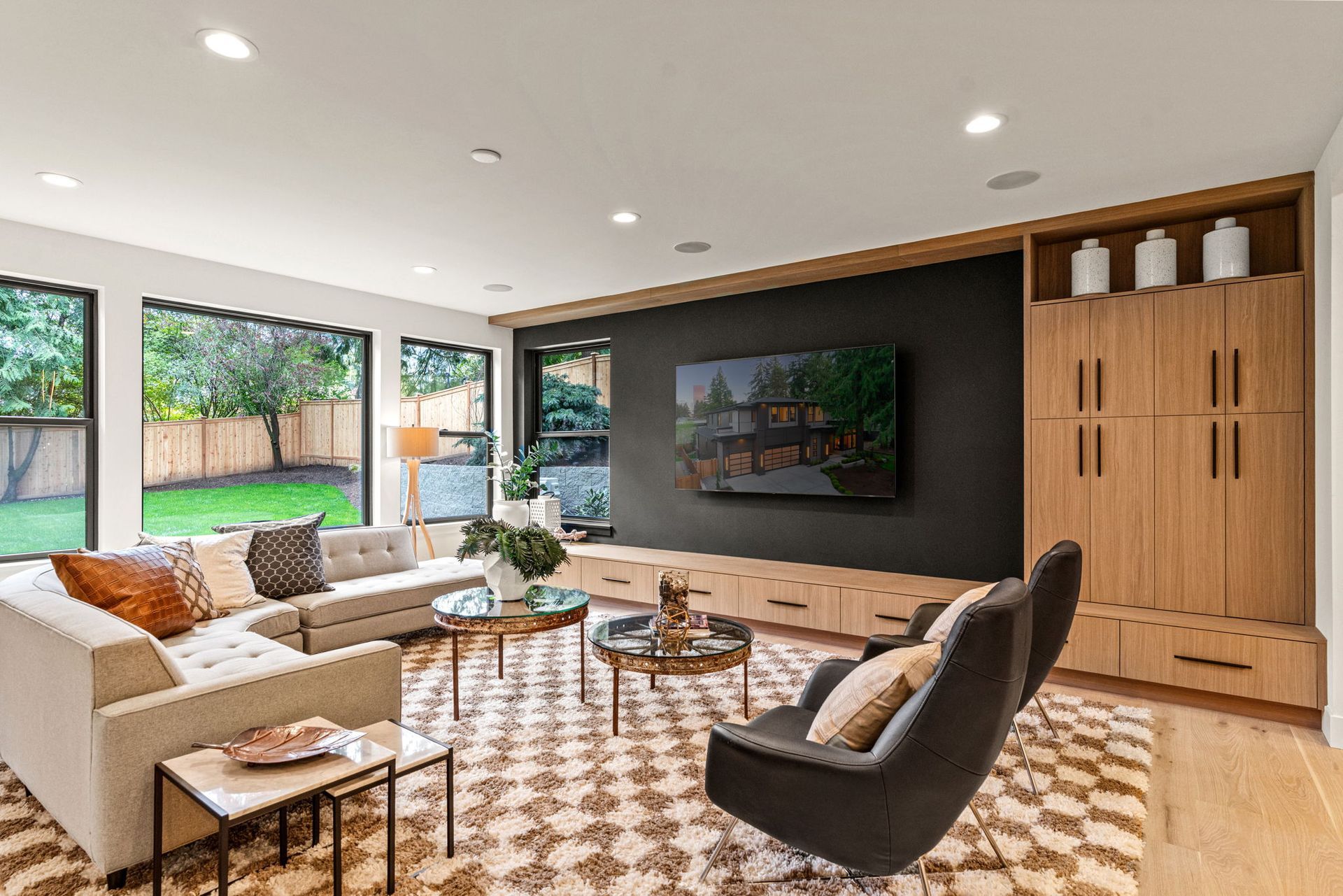 A modern living room with a large beige sectional, two dark armchairs, a patterned rug, and built-in light wood cabinetry.