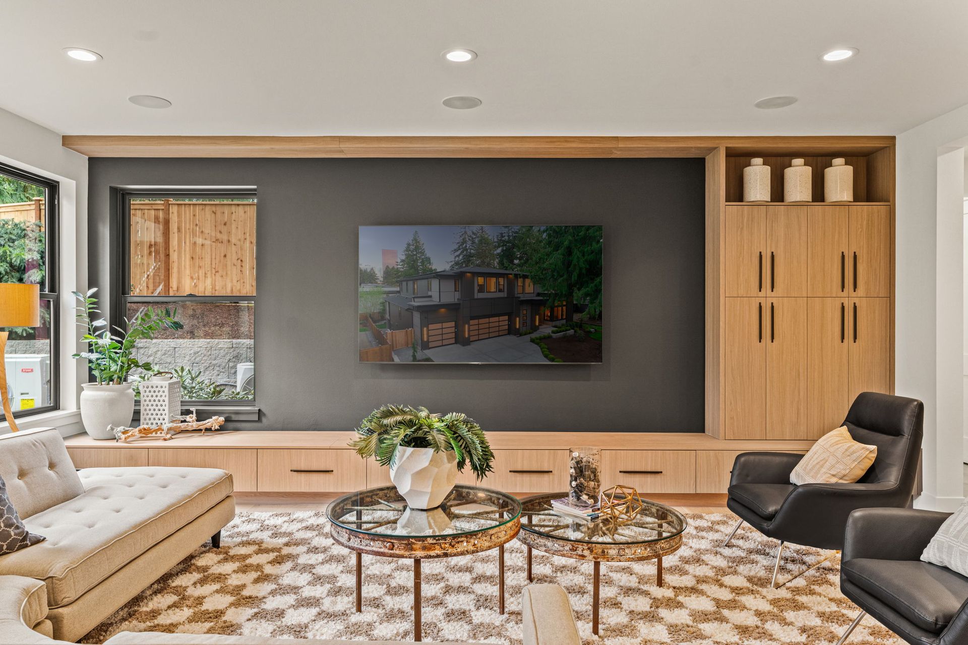 A modern living room with a gray accent wall, a wall-mounted TV, light wood cabinetry, two black chairs, and a sofa.