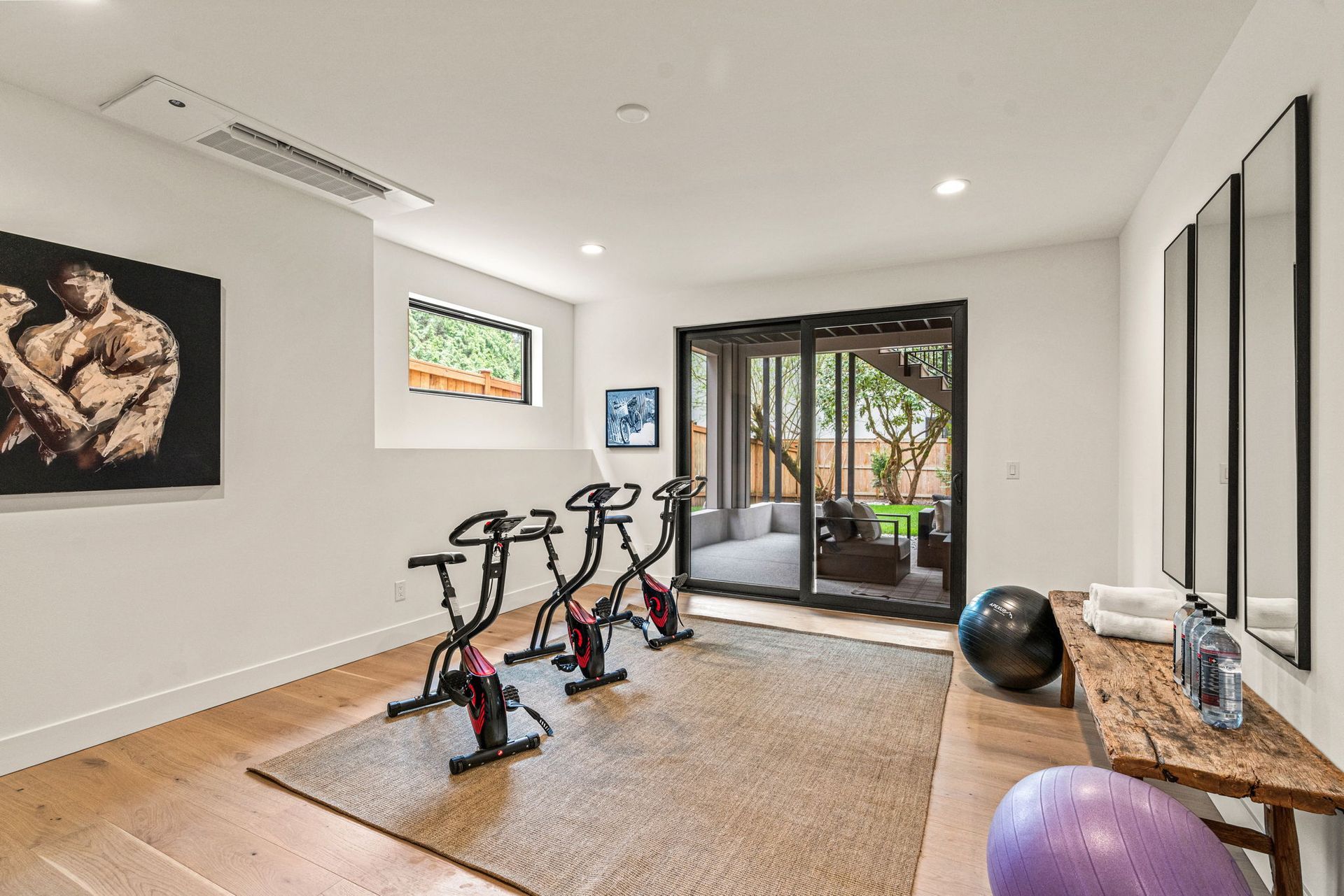 A modern two-story suburban house with a two-car glass garage, dark wood accents, and mature evergreen trees.