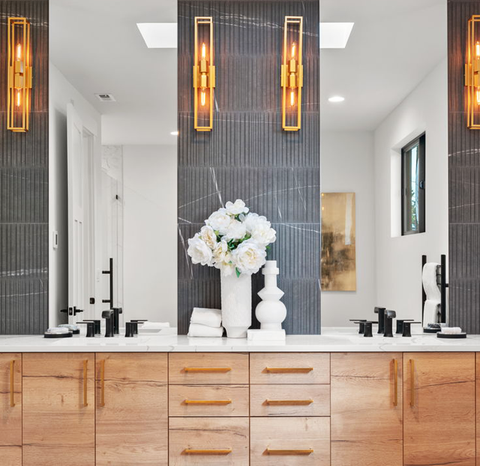 A bathroom with two sinks , two mirrors and a vase of flowers on the counter.