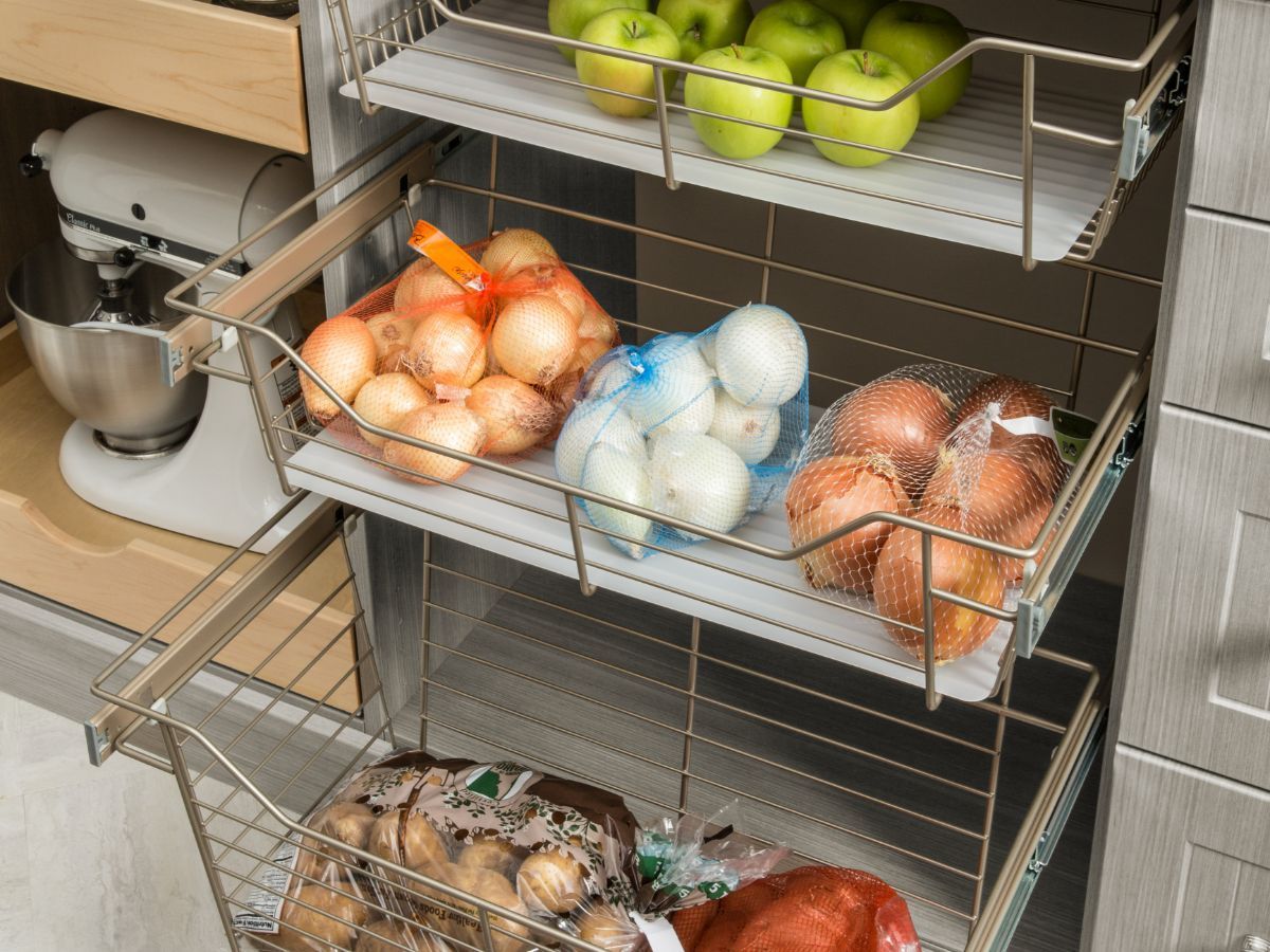 A kitchen drawer filled with fruits and vegetables including onions and apples.