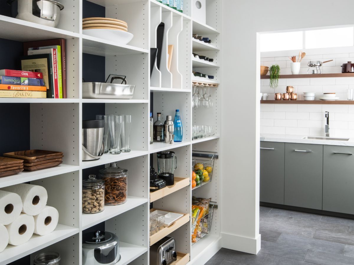 A pantry with lots of shelves and a kitchen in the background.