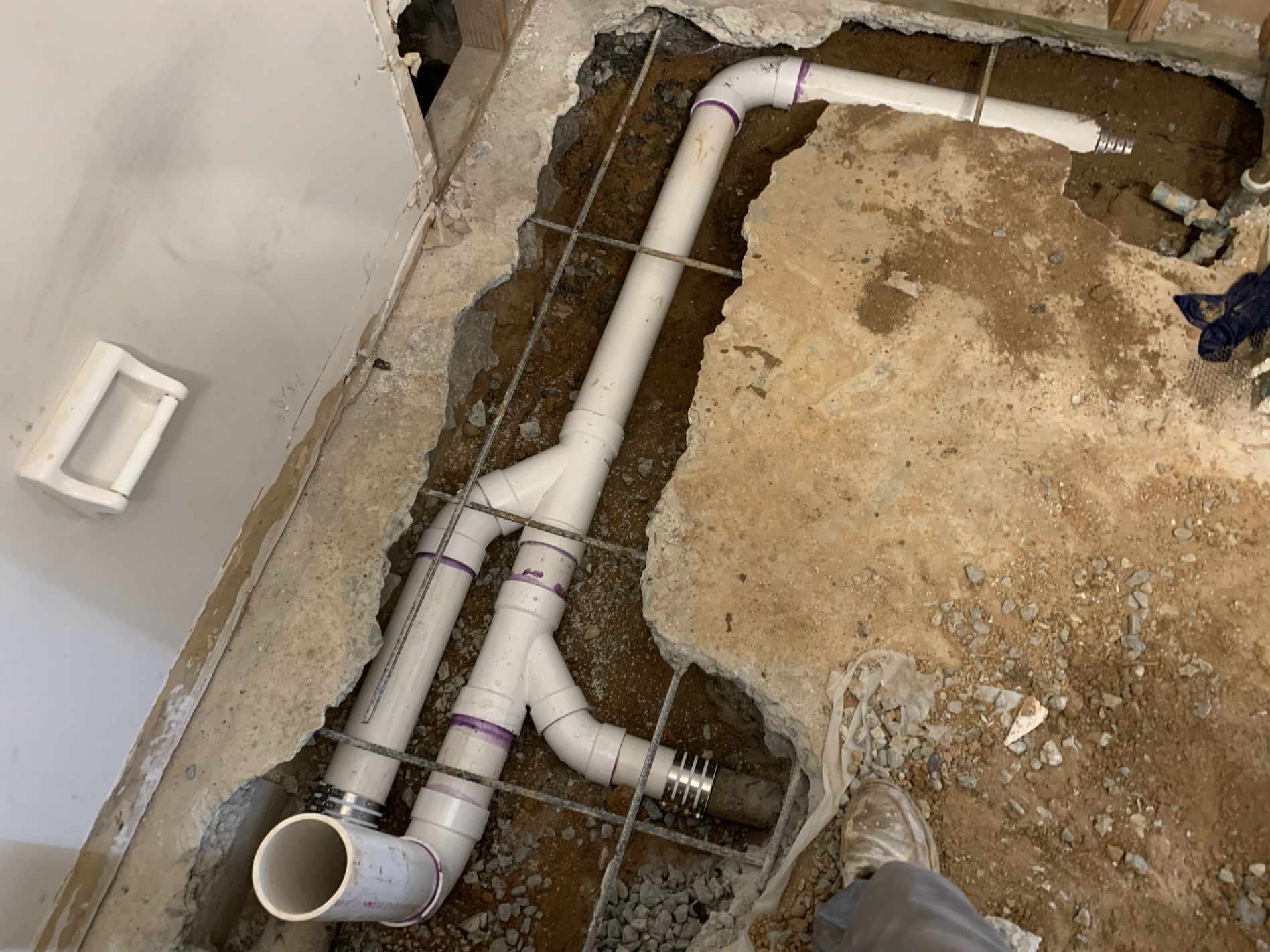 White PVC plumbing pipes installed in concrete floor, likely for a bathroom.