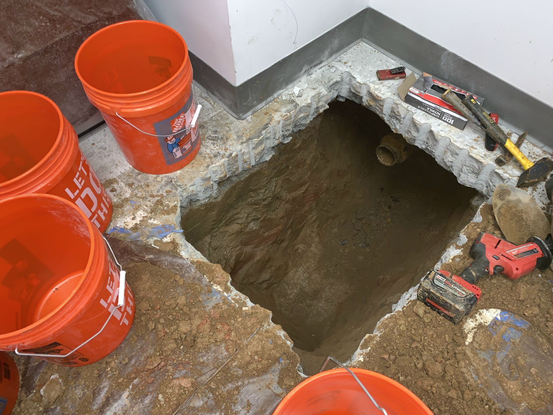 Hole in floor with dirt; orange buckets surround; construction tools nearby.