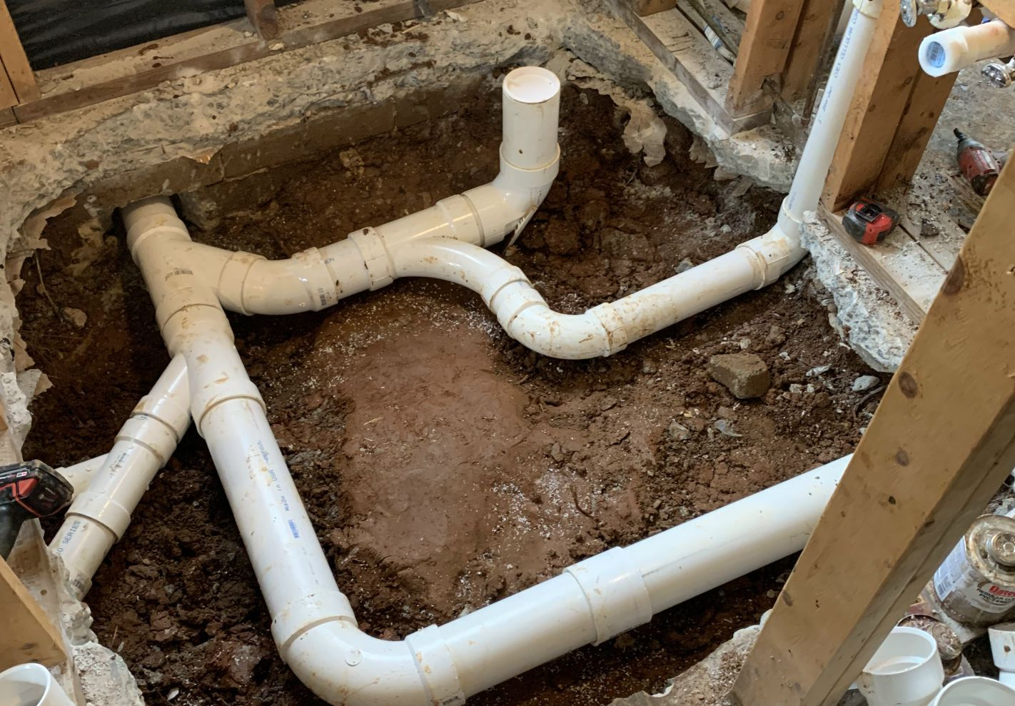 White PVC plumbing pipes installed in a dirt pit within a wood-framed structure.