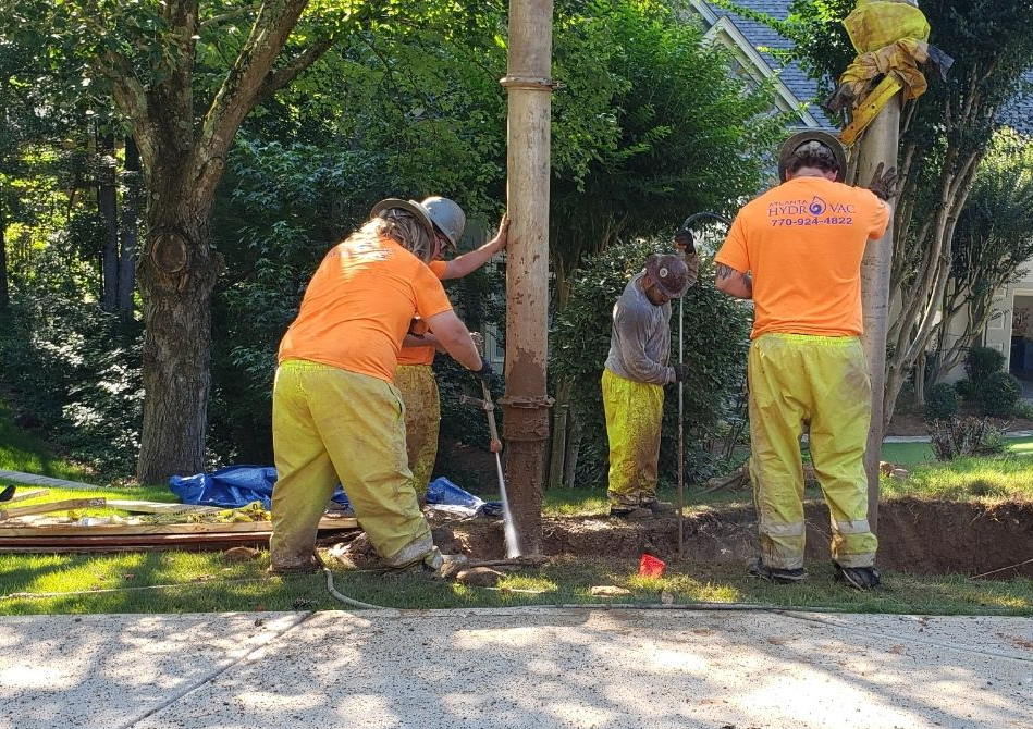 Construction workers in yellow safety gear working on a utility pole outdoors.