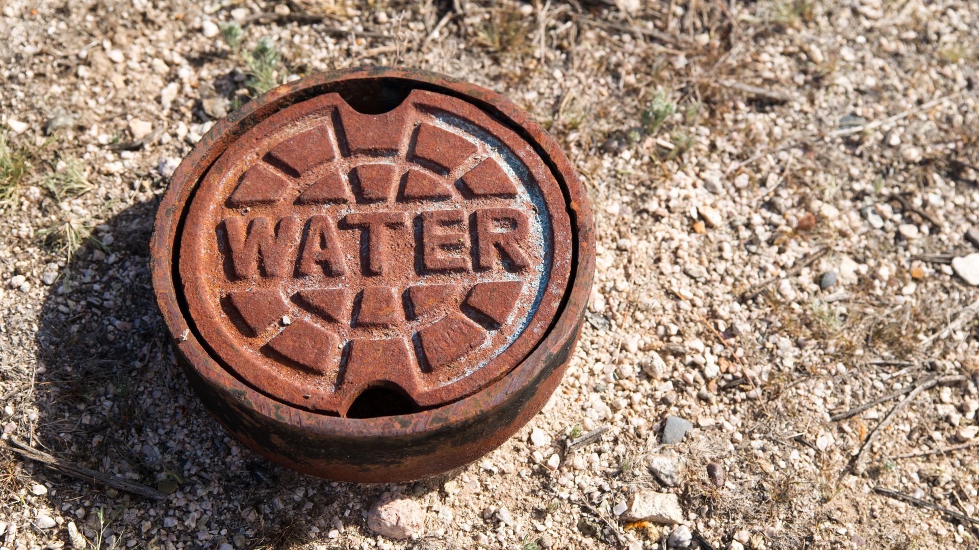 Rusty water access cover on gravel ground.