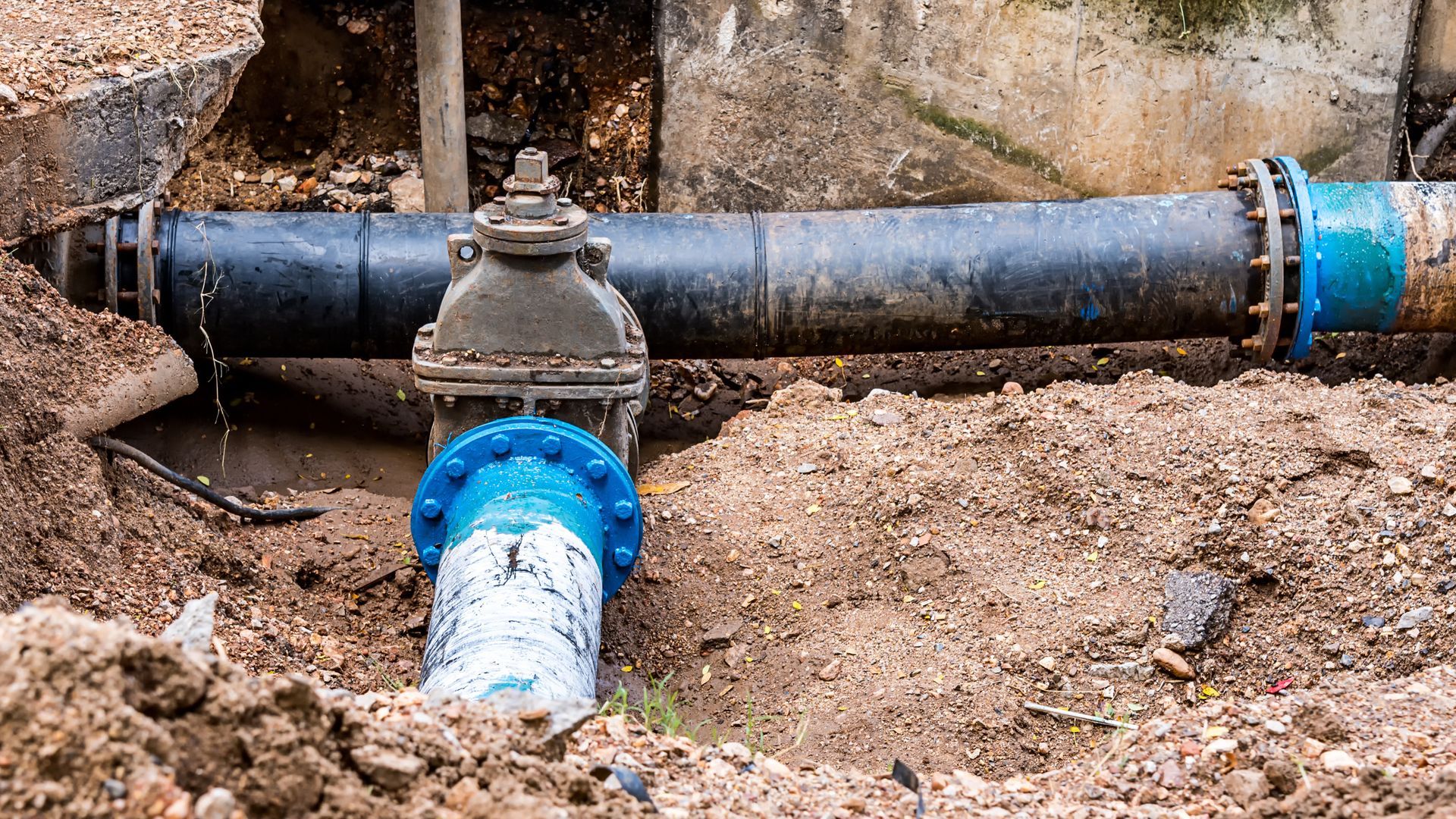 Water pipe repair, partially buried in dirt, with valve and blue fittings.